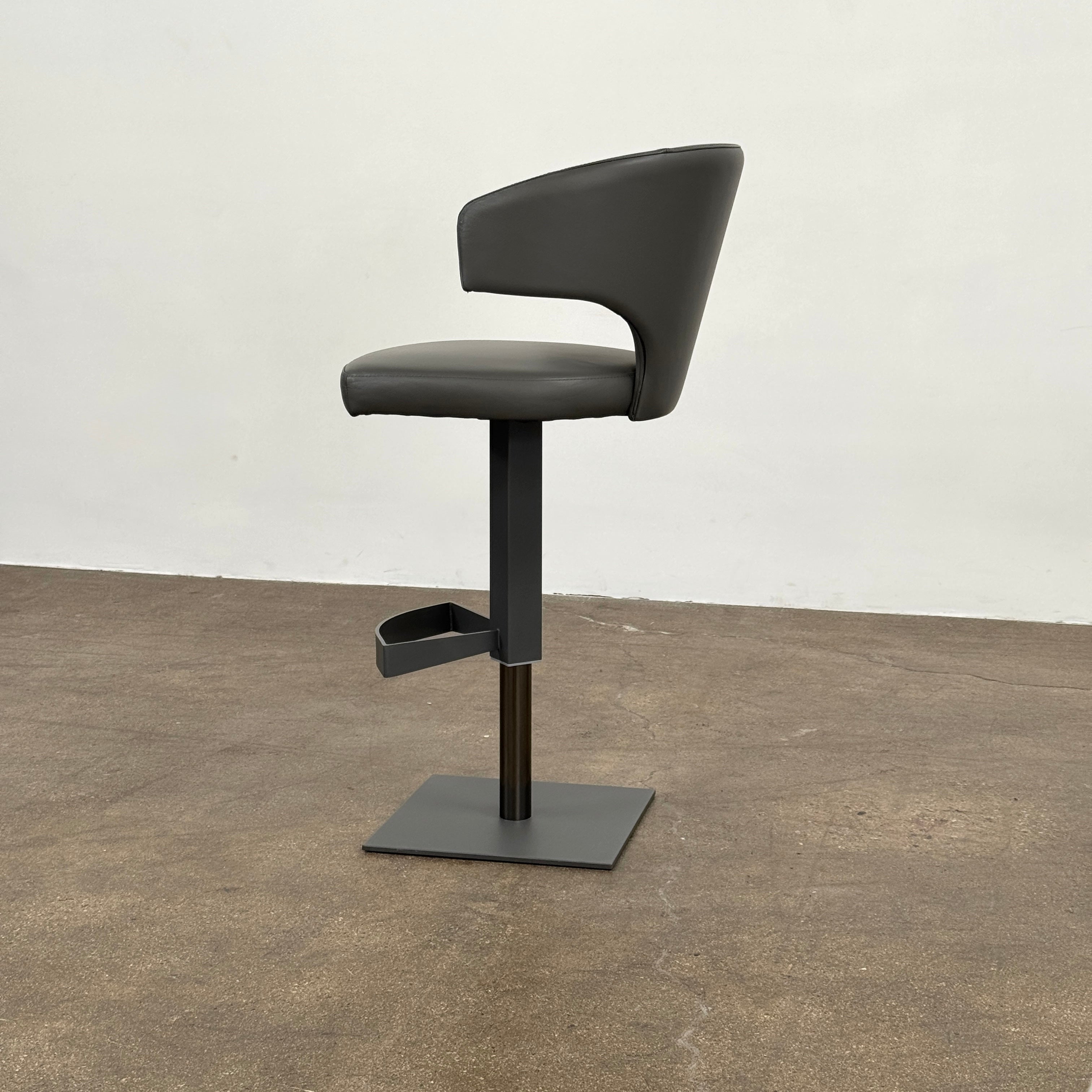 The Cantoni Wing Barstool by Cantoni features a modern black swivel design with a metal base, set on a brown concrete floor against a plain white wall.