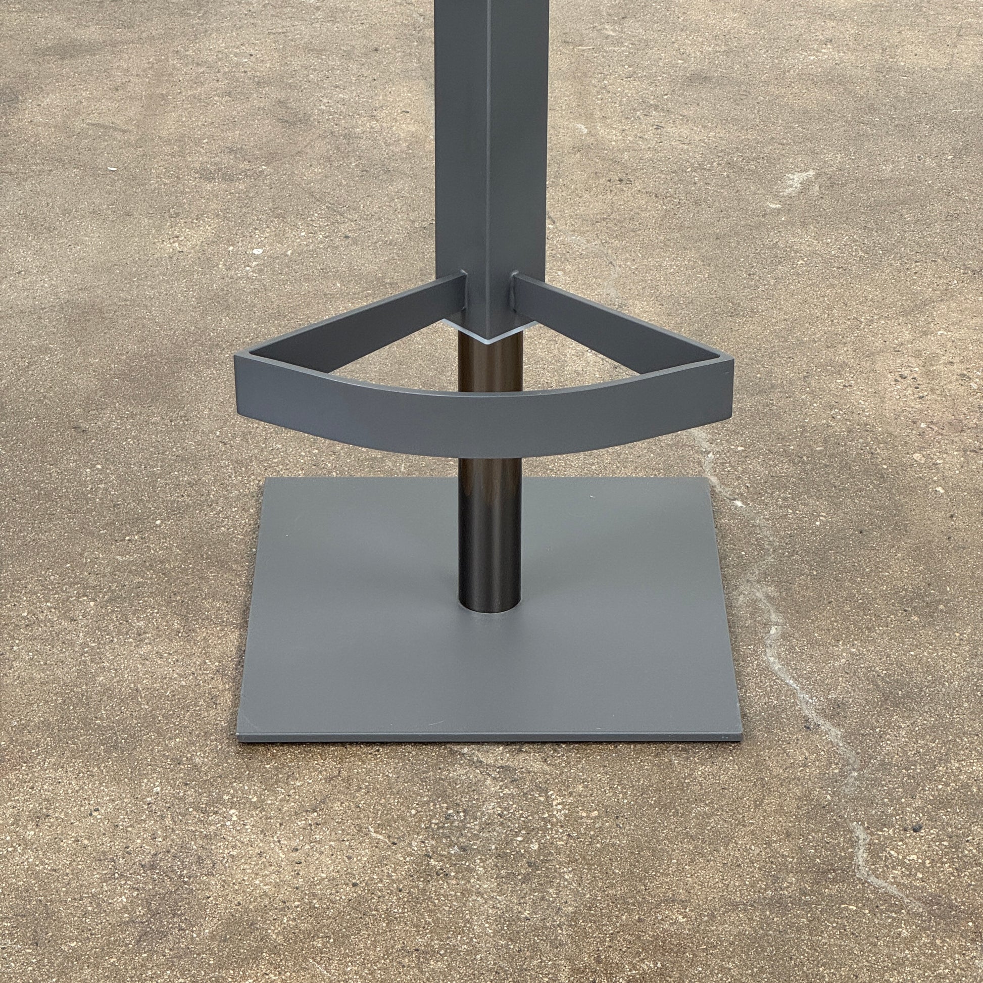 The Cantoni Wing Barstool by Cantoni features a modern black swivel design with a metal base, set on a brown concrete floor against a plain white wall.