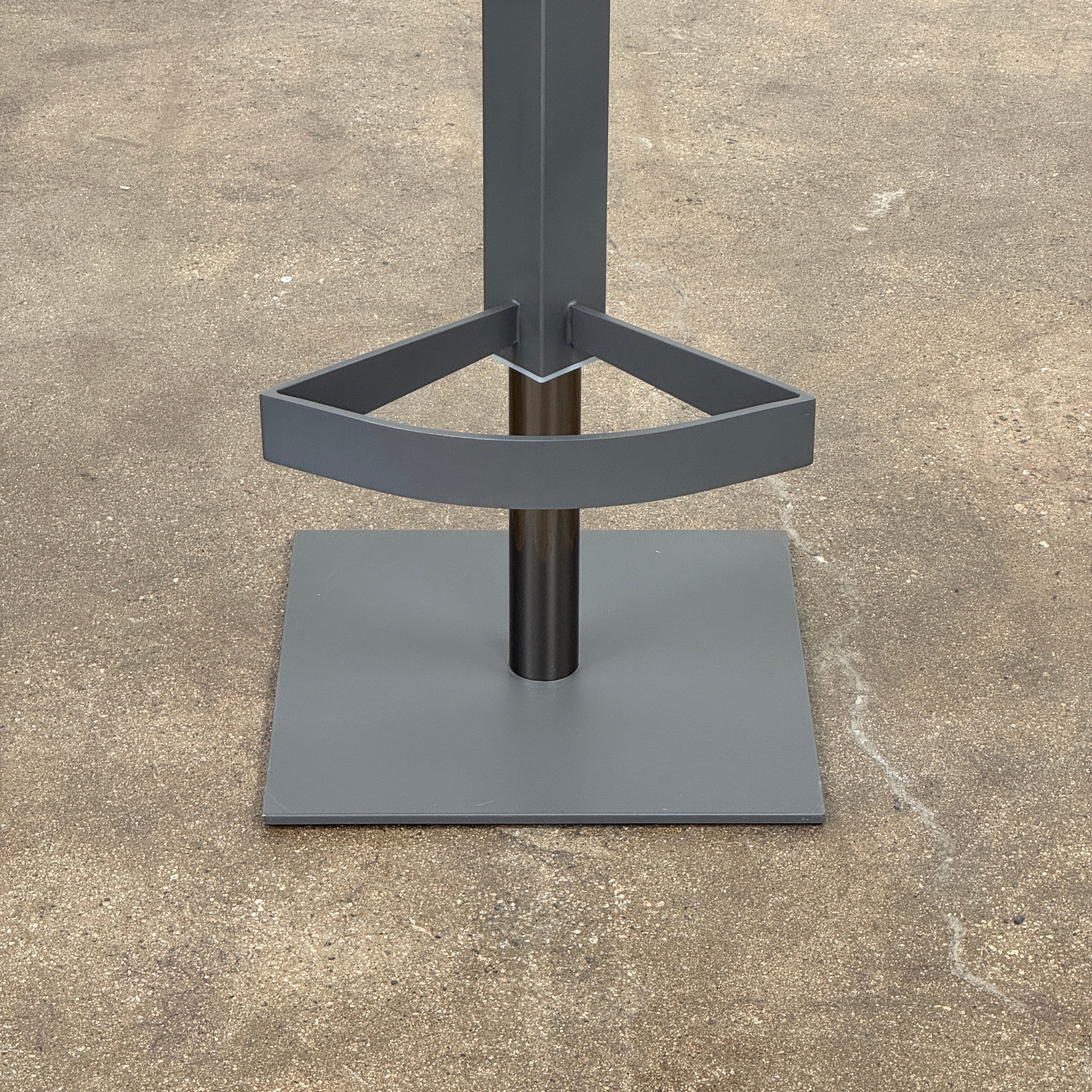 The Cantoni Wing Barstool by Cantoni features a modern black swivel design with a metal base, set on a brown concrete floor against a plain white wall.