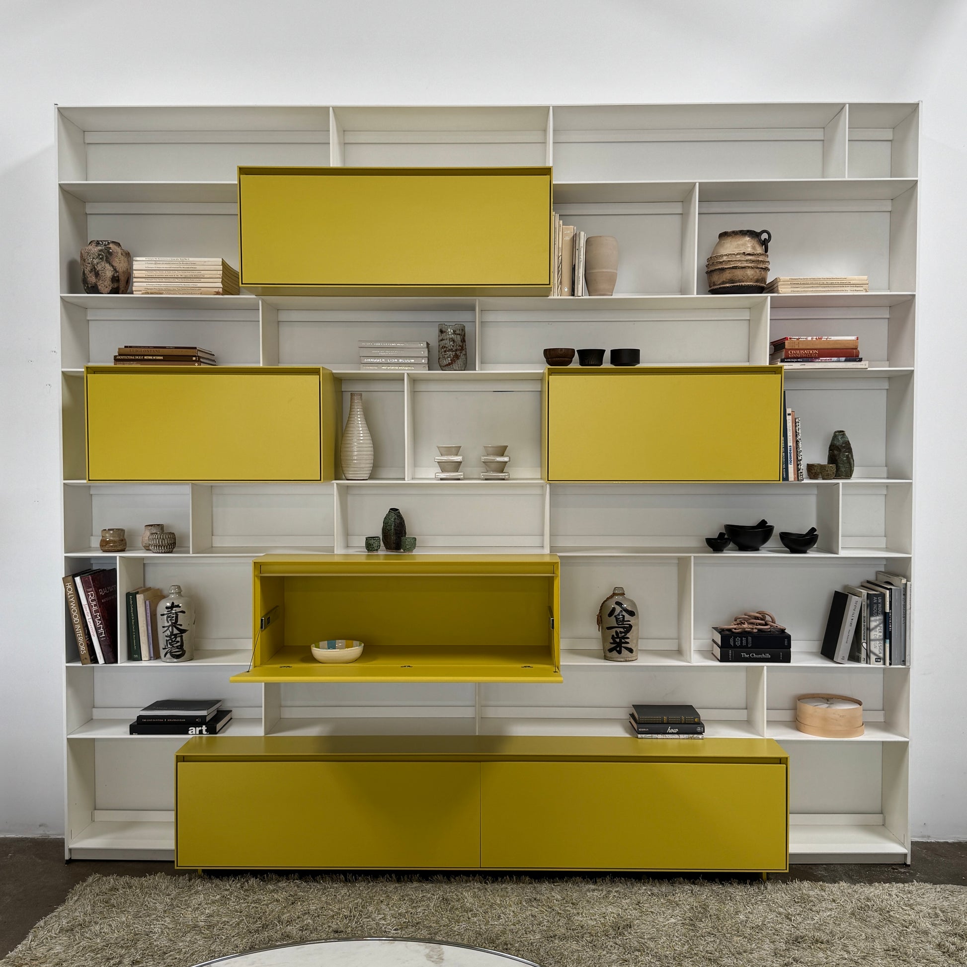 Close-up of a yellow cabinet door with a small paint chip on the bottom edge; black bowls and books are seen on a white shelf of the B&B Italia Flat C Wall Unit With Storage by B&B Italia, combining style and function.