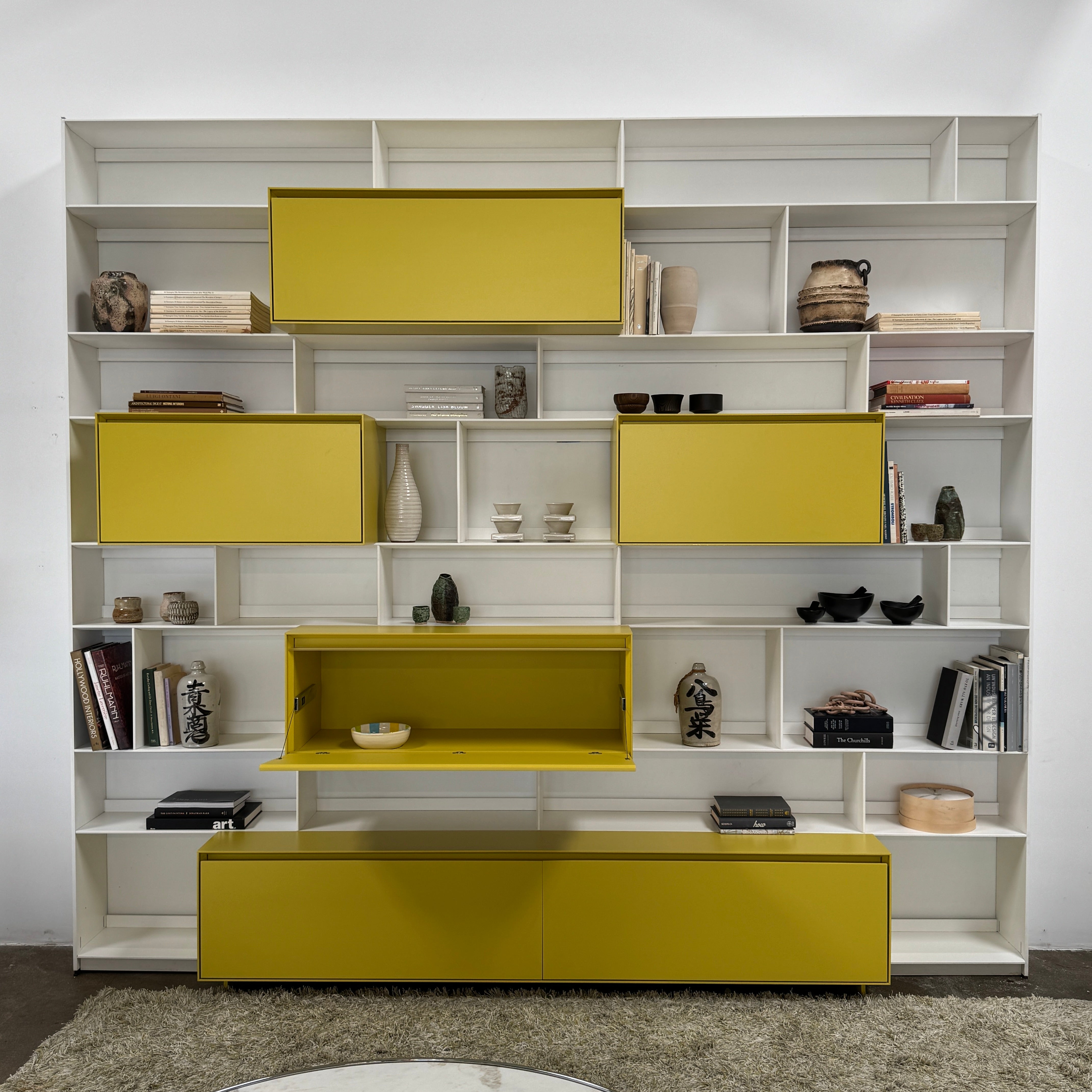 Close-up of a yellow cabinet door with a small paint chip on the bottom edge; black bowls and books are seen on a white shelf of the B&B Italia Flat C Wall Unit With Storage by B&B Italia, combining style and function.