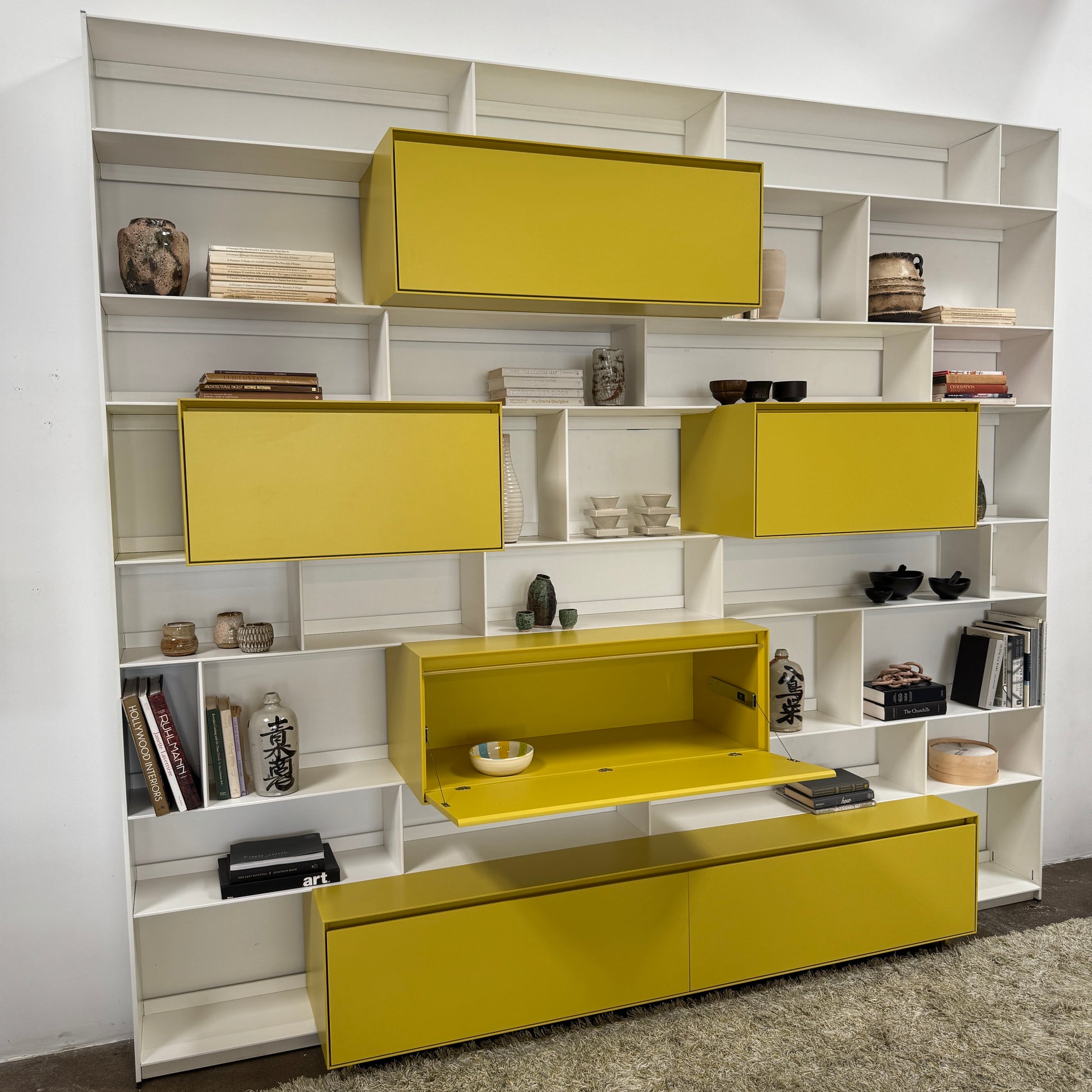 Close-up of a yellow cabinet door with a small paint chip on the bottom edge; black bowls and books are seen on a white shelf of the B&B Italia Flat C Wall Unit With Storage by B&B Italia, combining style and function.