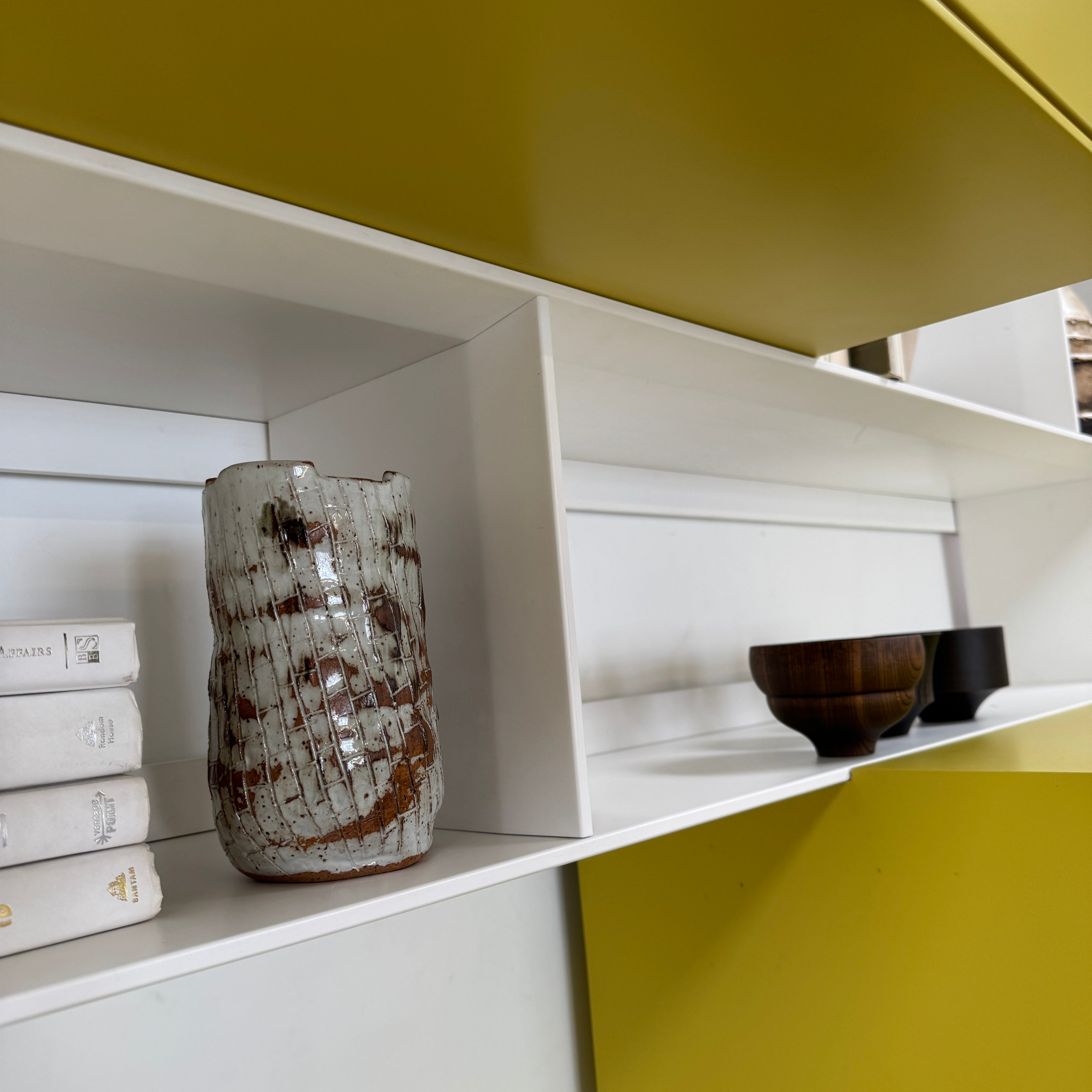 Close-up of a yellow cabinet door with a small paint chip on the bottom edge; black bowls and books are seen on a white shelf of the B&B Italia Flat C Wall Unit With Storage by B&B Italia, combining style and function.