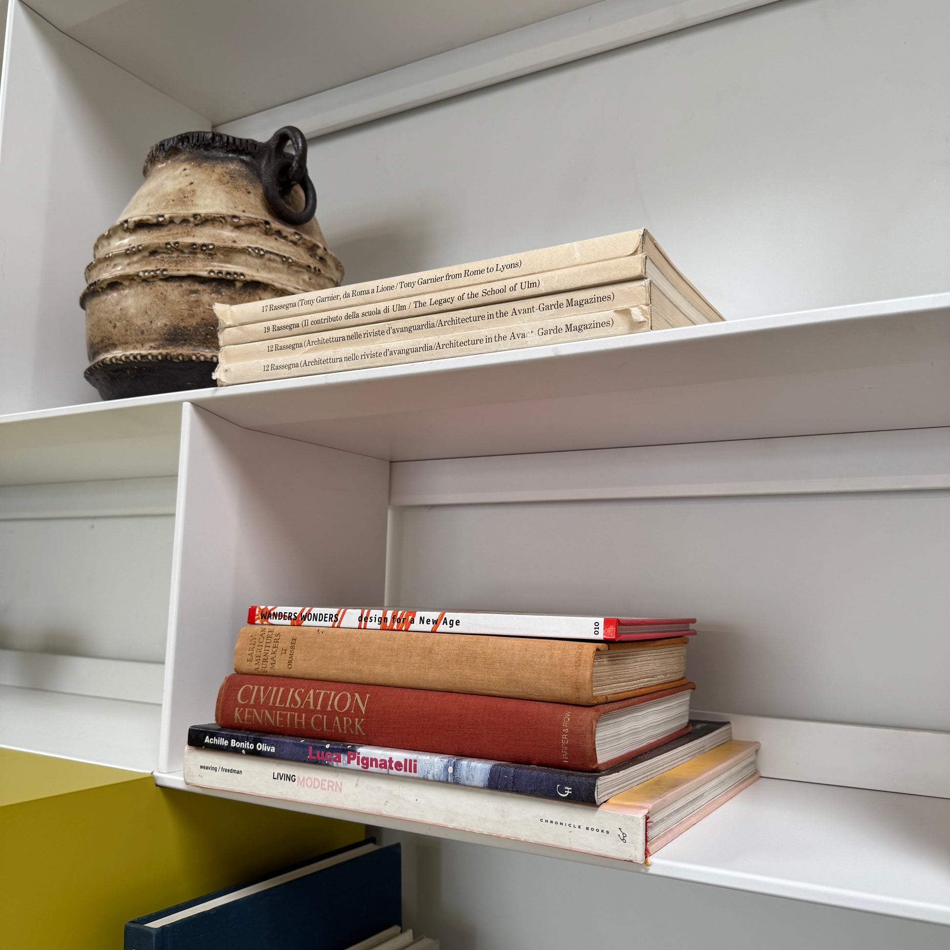 Close-up of a yellow cabinet door with a small paint chip on the bottom edge; black bowls and books are seen on a white shelf of the B&B Italia Flat C Wall Unit With Storage by B&B Italia, combining style and function.