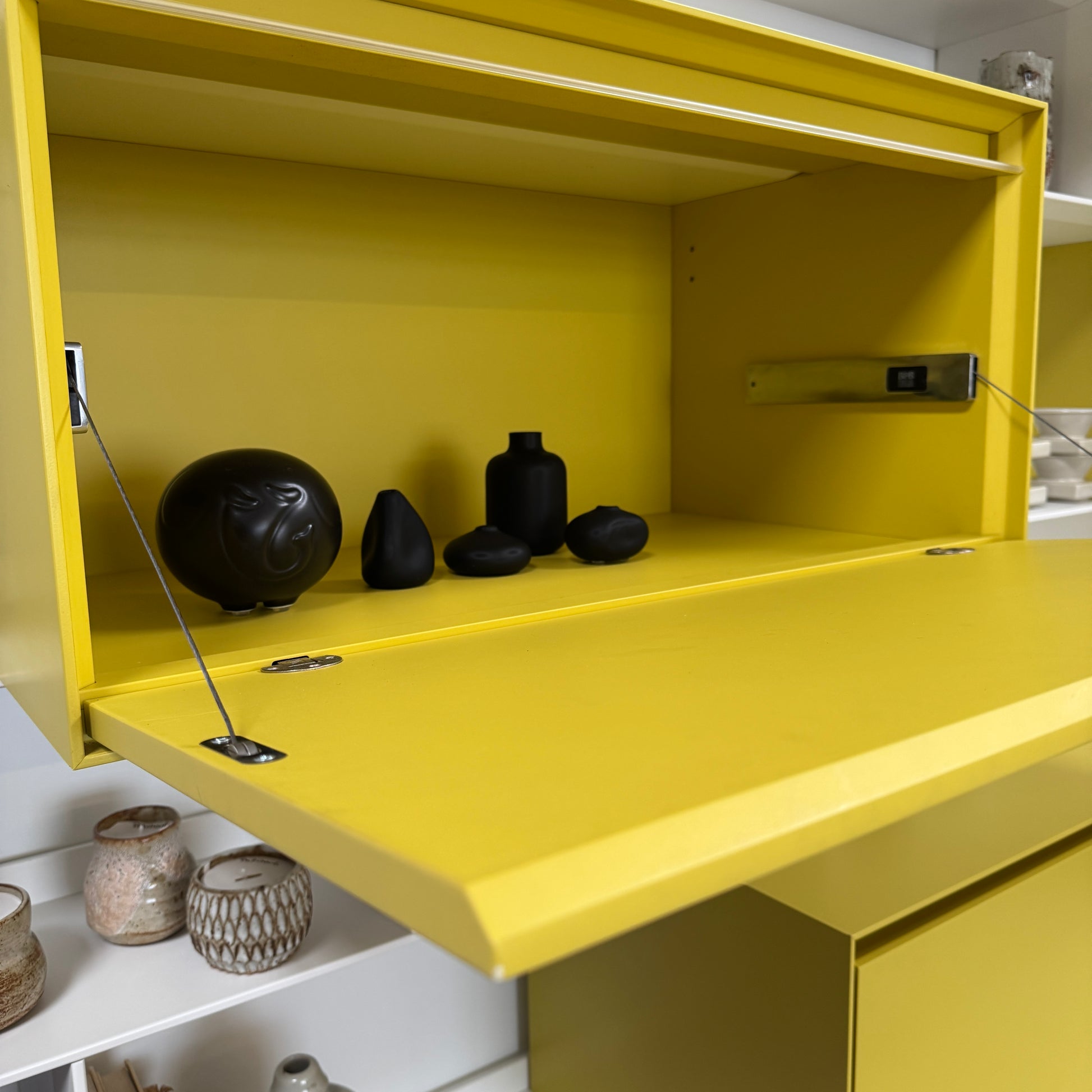 Close-up of a yellow cabinet door with a small paint chip on the bottom edge; black bowls and books are seen on a white shelf of the B&B Italia Flat C Wall Unit With Storage by B&B Italia, combining style and function.