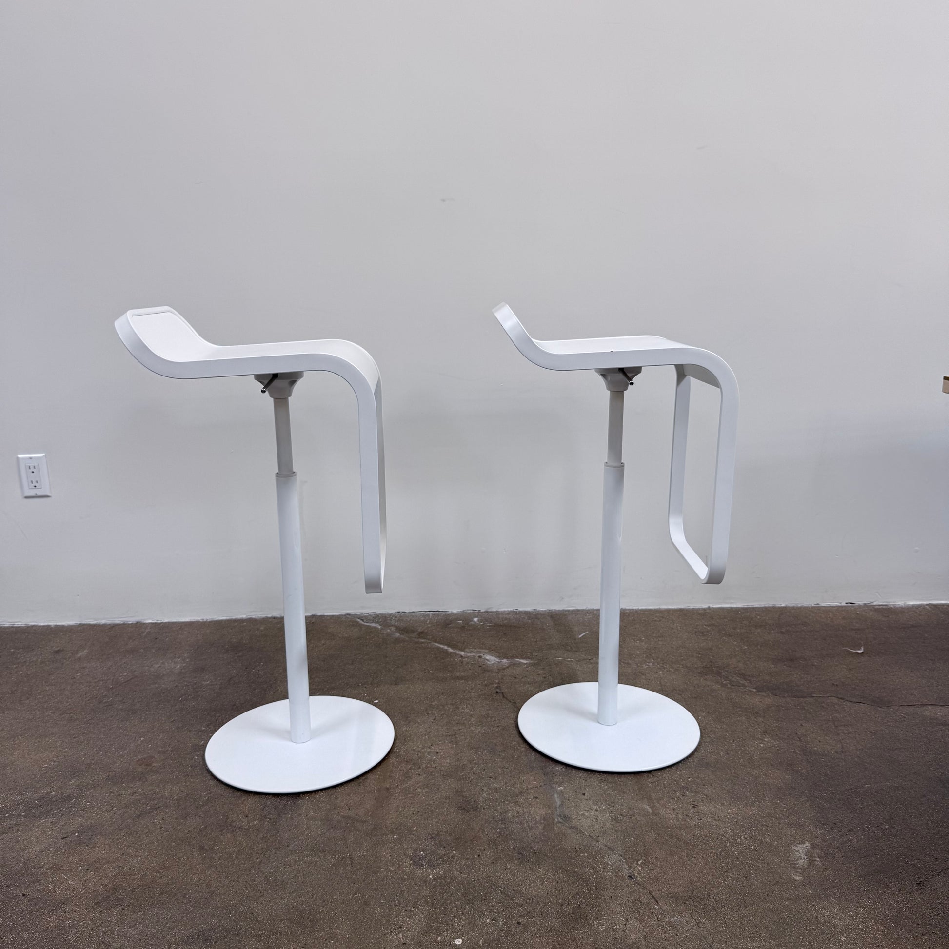 Two white LEM Piston Stools by La Palma featuring pedestal bases and rectangular footrests.