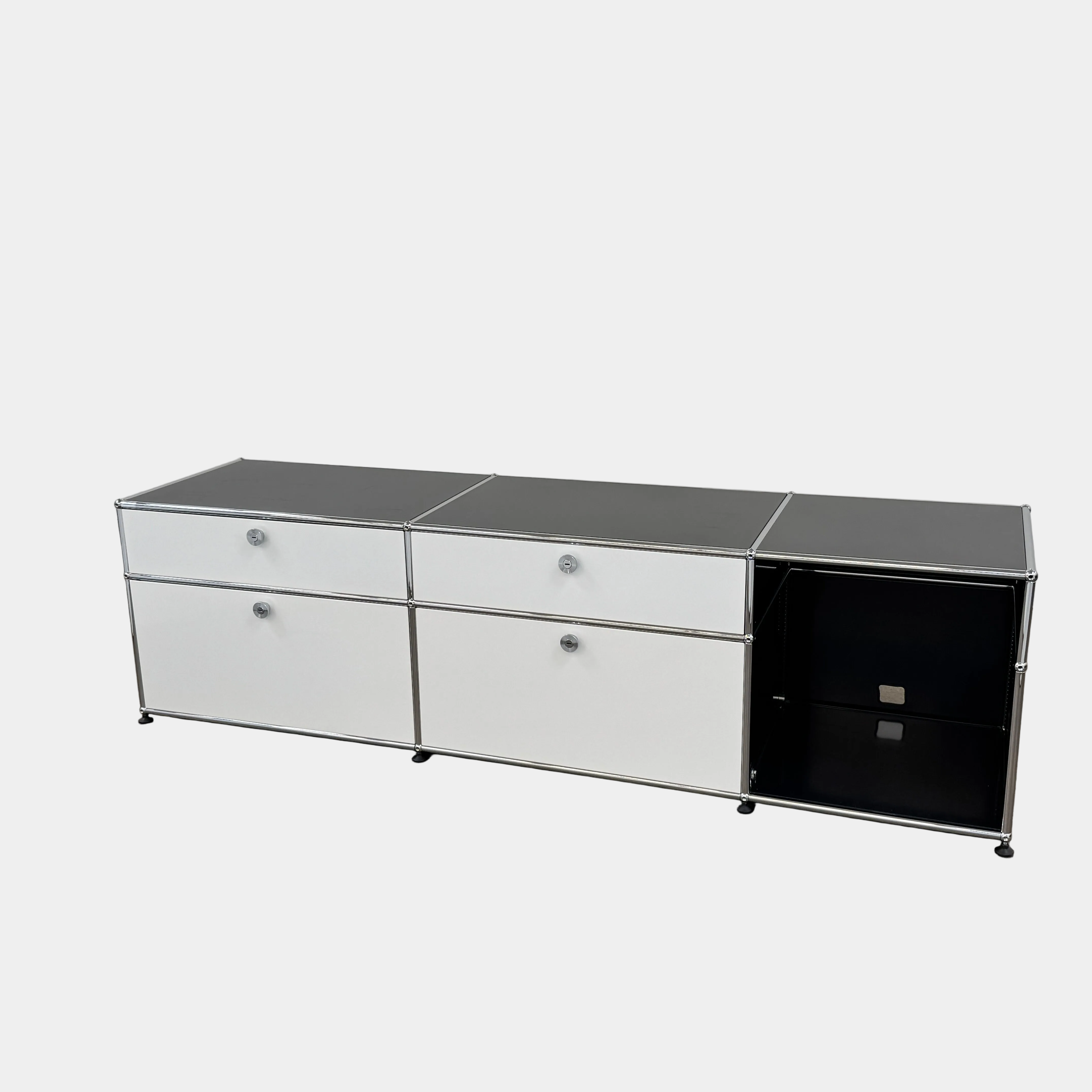 The USM Haller Cabinet / Console by Fritz Haller and Paul Schaerer for USM Haller features black and white panels, a metal frame, drawers, and open shelves—showcasing timeless modular design near a beige wall on concrete flooring.