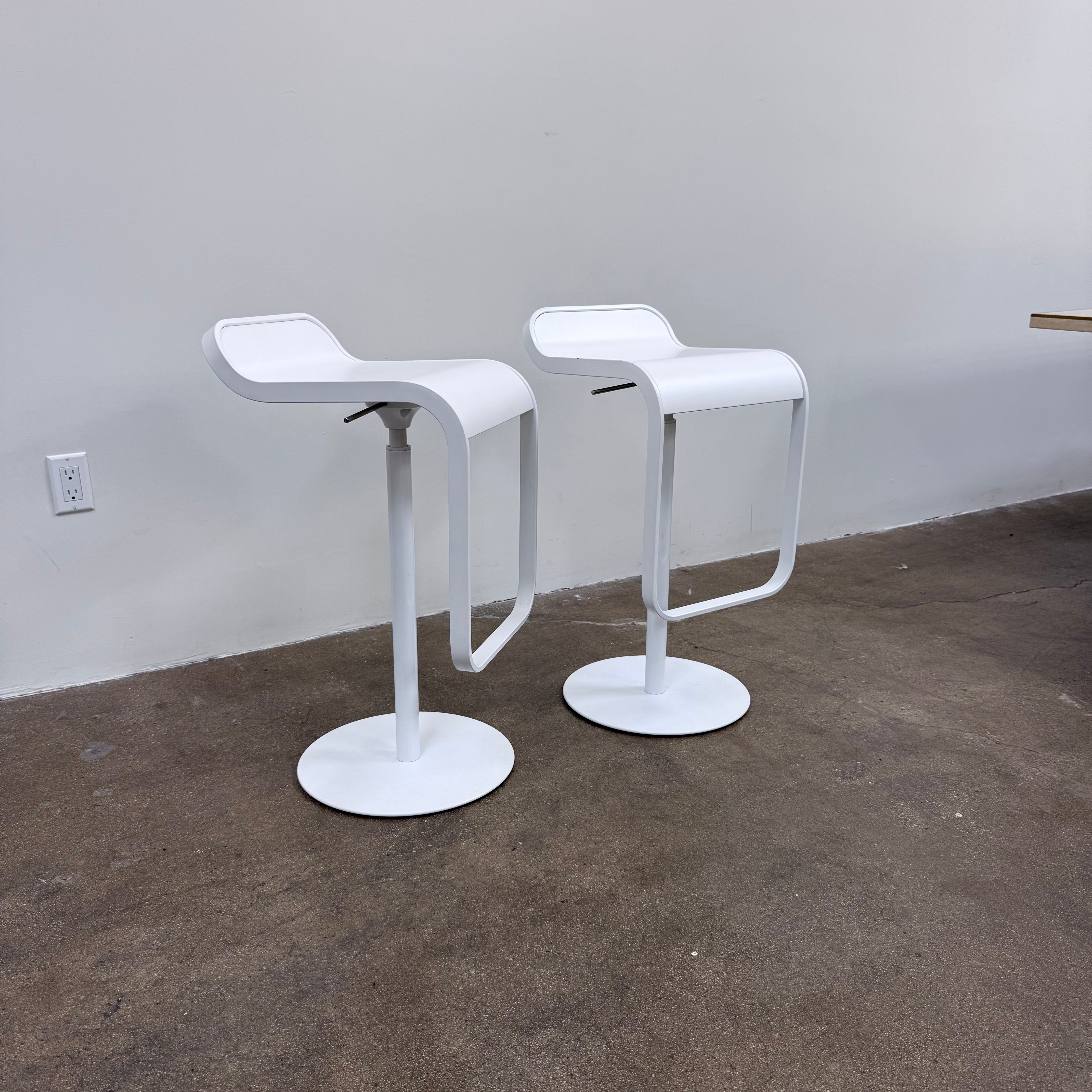 Two white LEM Piston Stools by La Palma featuring pedestal bases and rectangular footrests.
