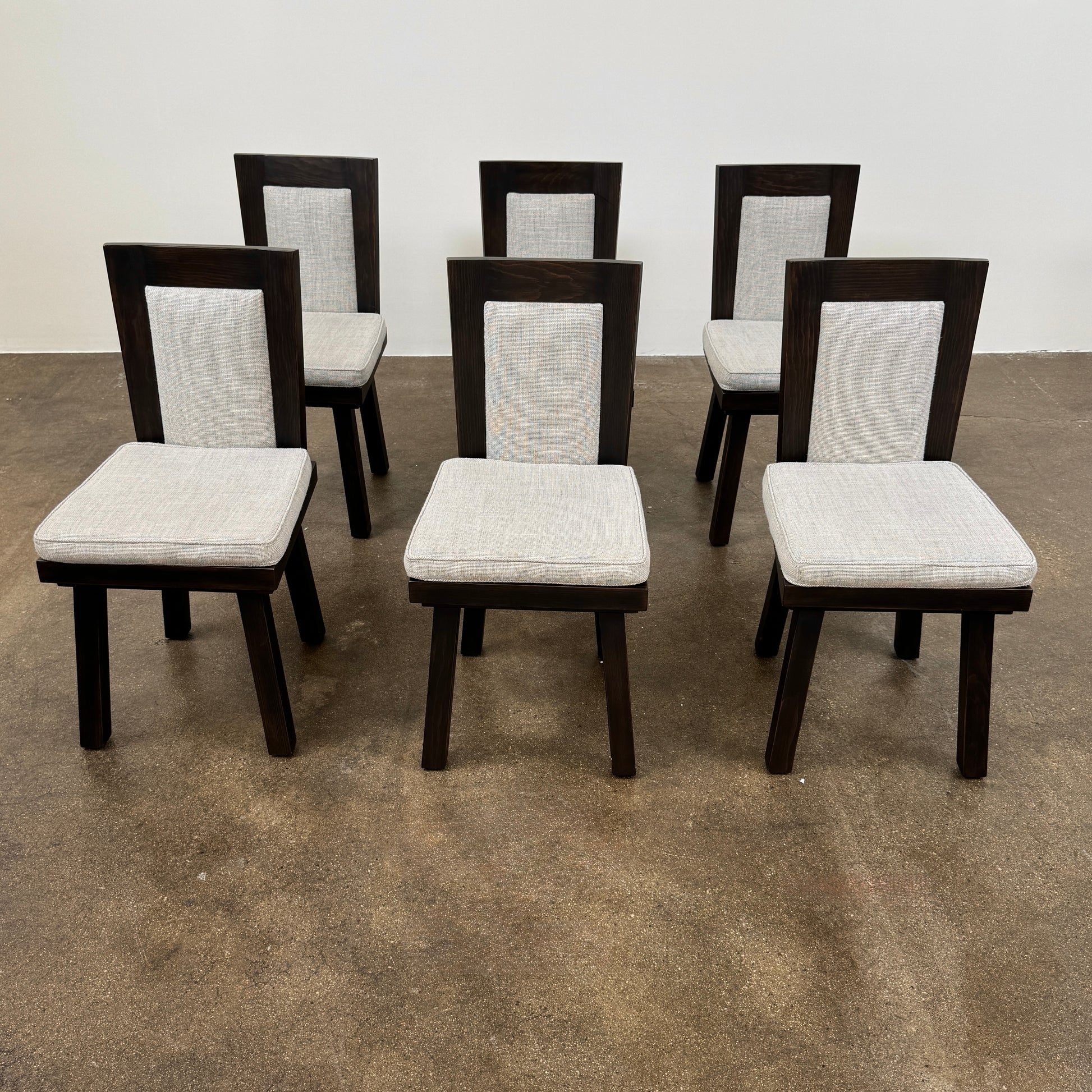 Six Waldo's Designs Custom Pine Dining Chairs (Set of 6) with light upholstered seats and backs are arranged in two rows on a bare concrete floor against a plain white wall.
