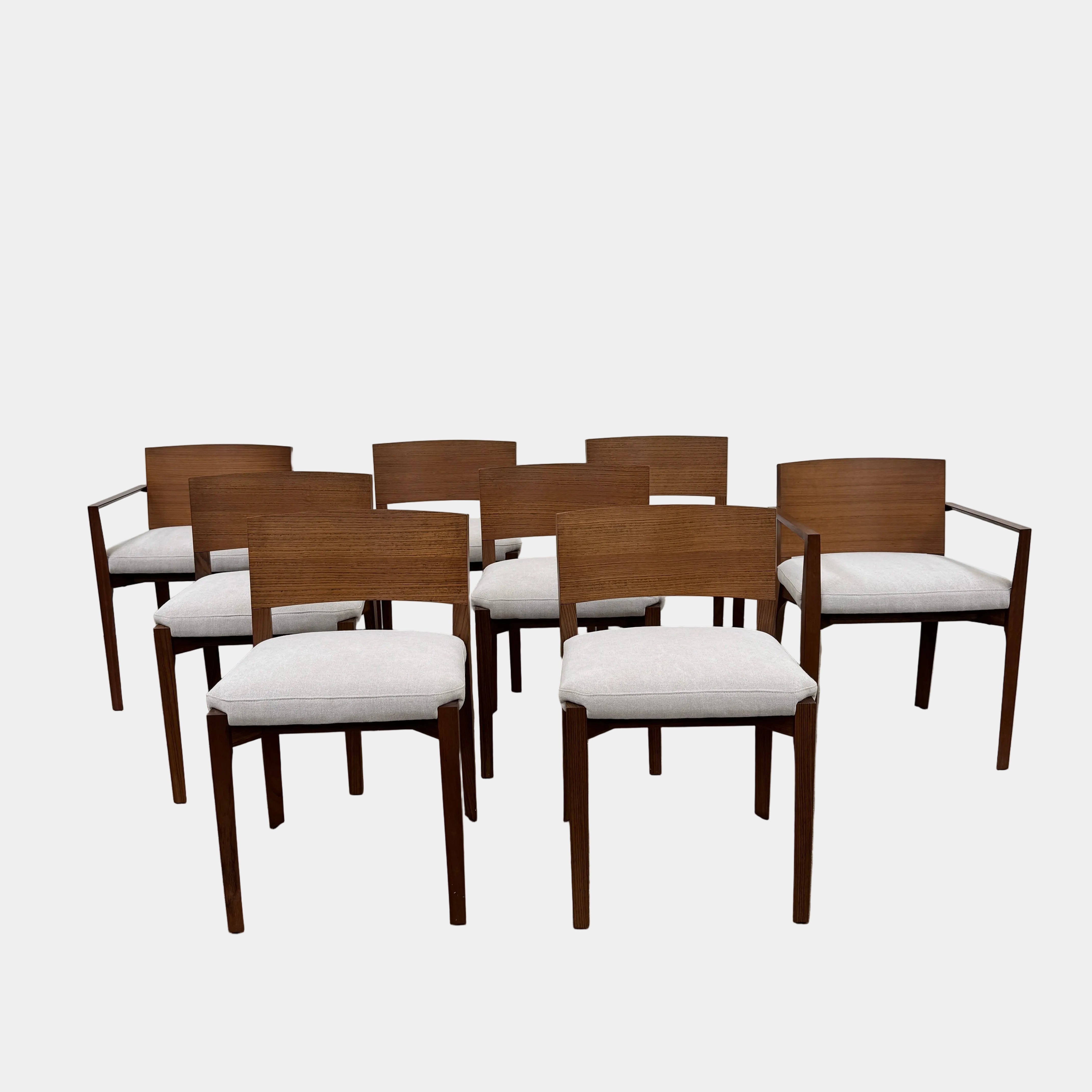 A set of 8 Porro Lario dining chairs by Porro, featuring minimalist armrests and light-cushioned seats, sits on a concrete floor against a plain white wall, reflecting refined contemporary style.