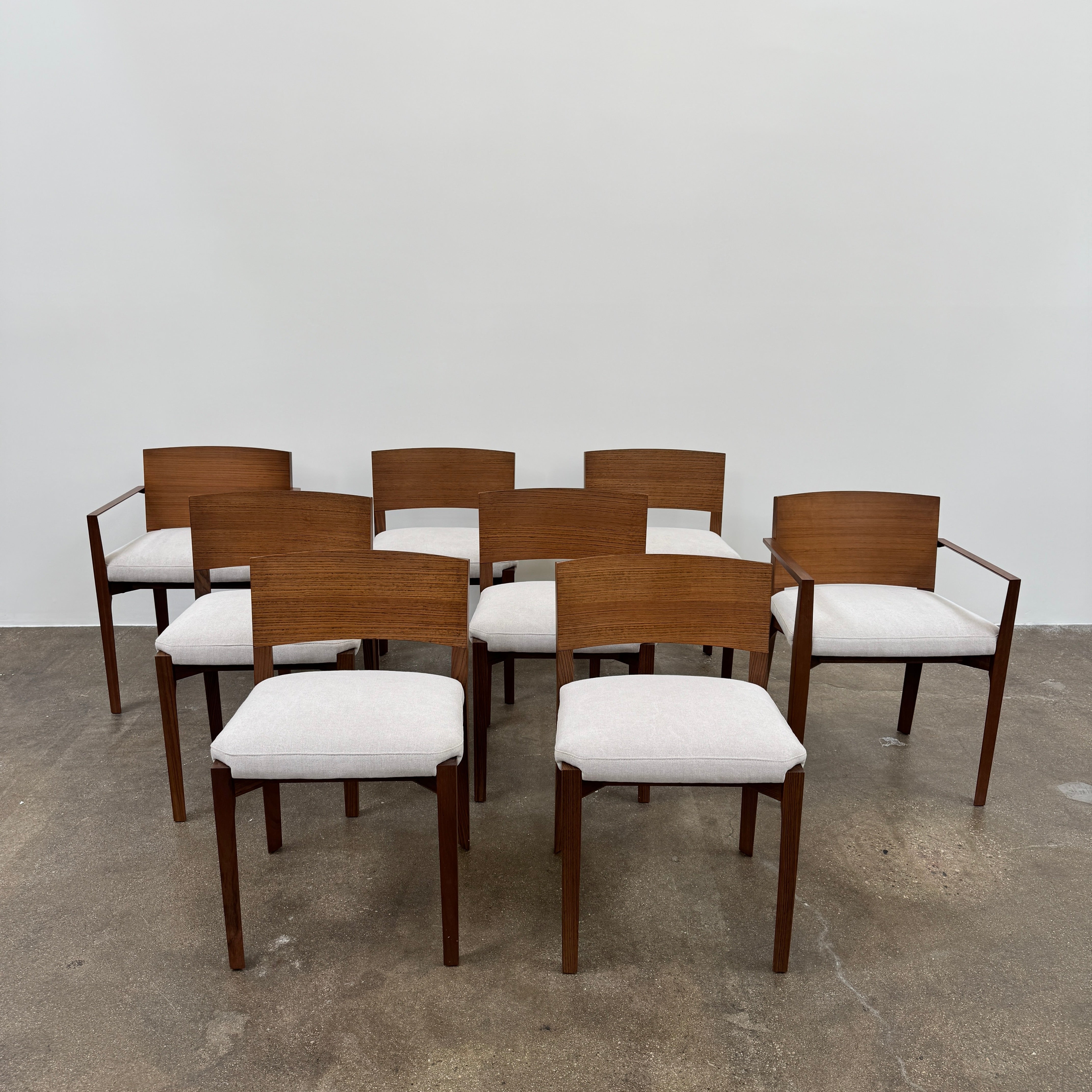 A set of 8 Porro Lario dining chairs by Porro, featuring minimalist armrests and light-cushioned seats, sits on a concrete floor against a plain white wall, reflecting refined contemporary style.