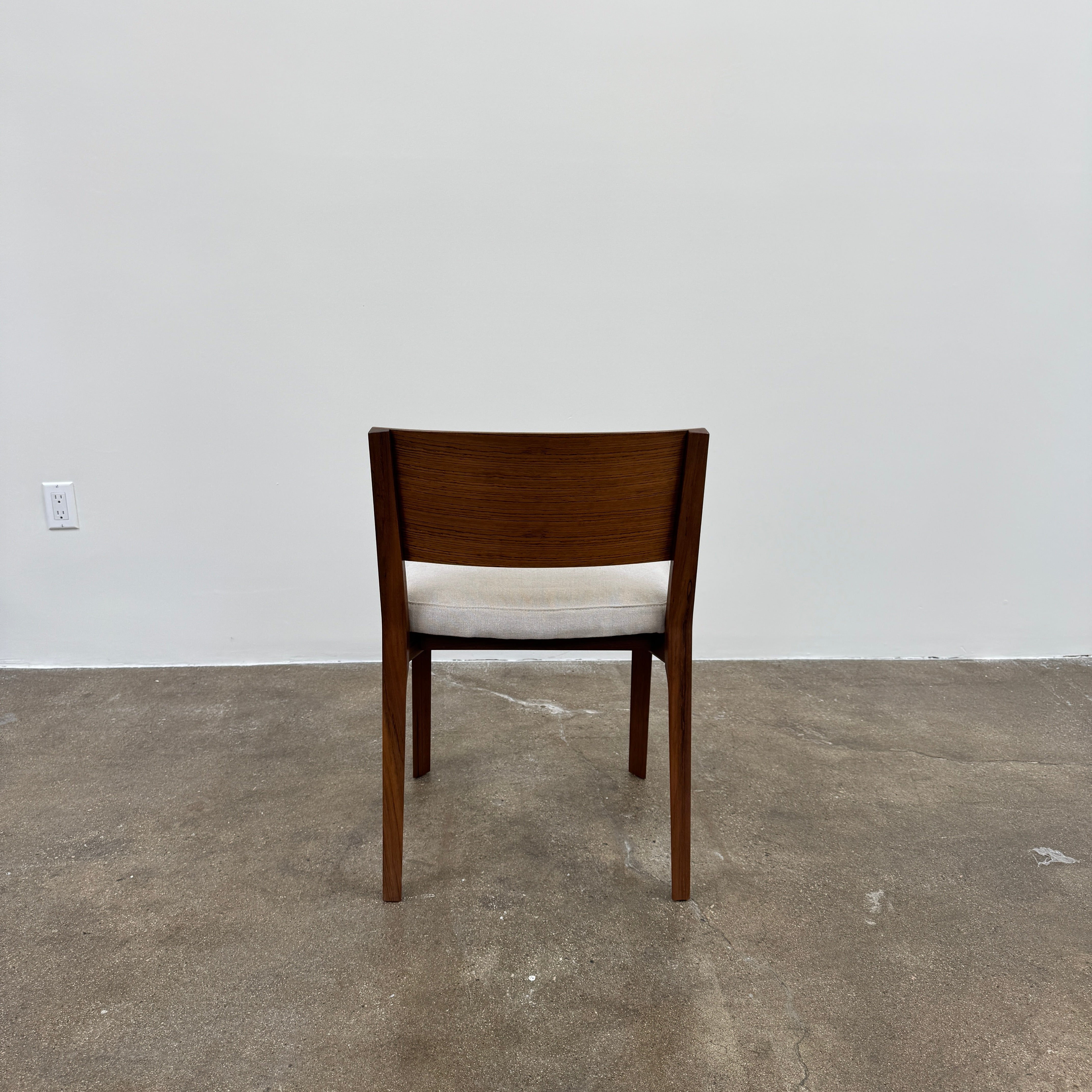 A set of 8 Porro Lario dining chairs by Porro, featuring minimalist armrests and light-cushioned seats, sits on a concrete floor against a plain white wall, reflecting refined contemporary style.