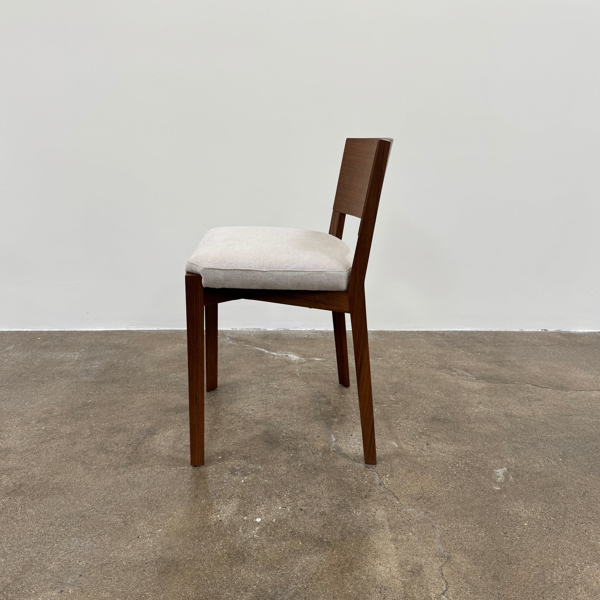 A set of 8 Porro Lario dining chairs by Porro, featuring minimalist armrests and light-cushioned seats, sits on a concrete floor against a plain white wall, reflecting refined contemporary style.