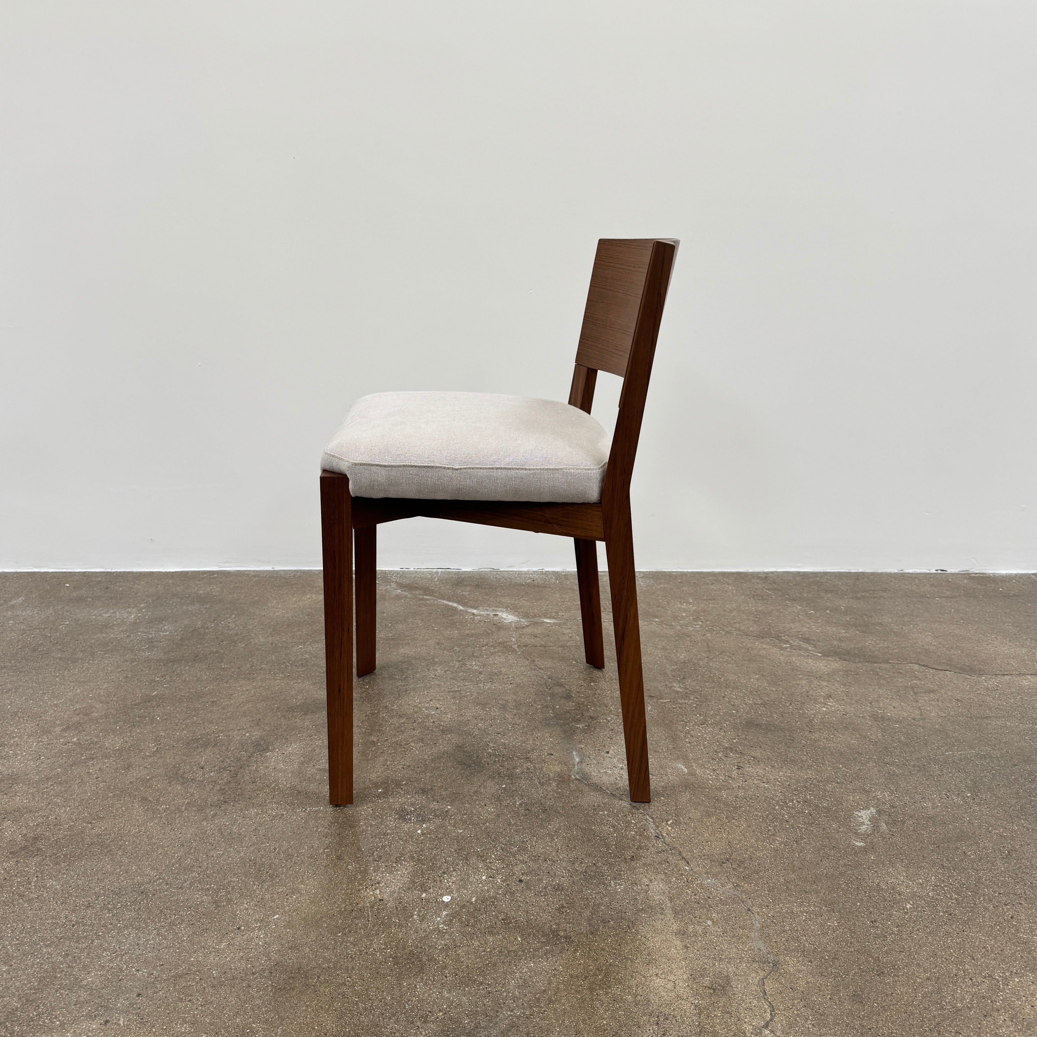 A set of 8 Porro Lario dining chairs by Porro, featuring minimalist armrests and light-cushioned seats, sits on a concrete floor against a plain white wall, reflecting refined contemporary style.