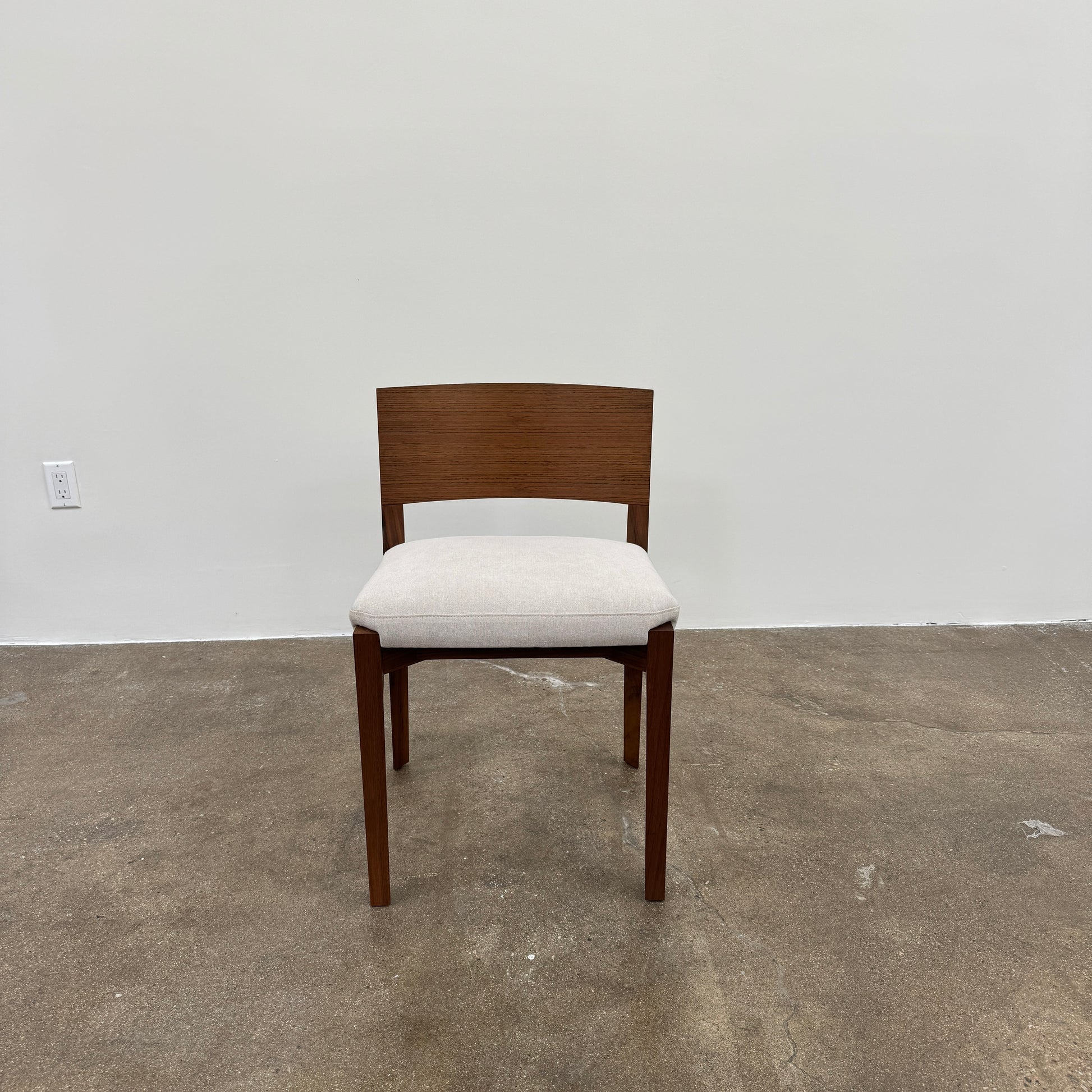 A set of 8 Porro Lario dining chairs by Porro, featuring minimalist armrests and light-cushioned seats, sits on a concrete floor against a plain white wall, reflecting refined contemporary style.