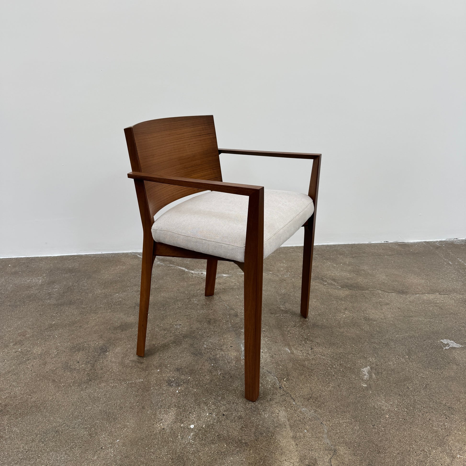 A set of 8 Porro Lario dining chairs by Porro, featuring minimalist armrests and light-cushioned seats, sits on a concrete floor against a plain white wall, reflecting refined contemporary style.