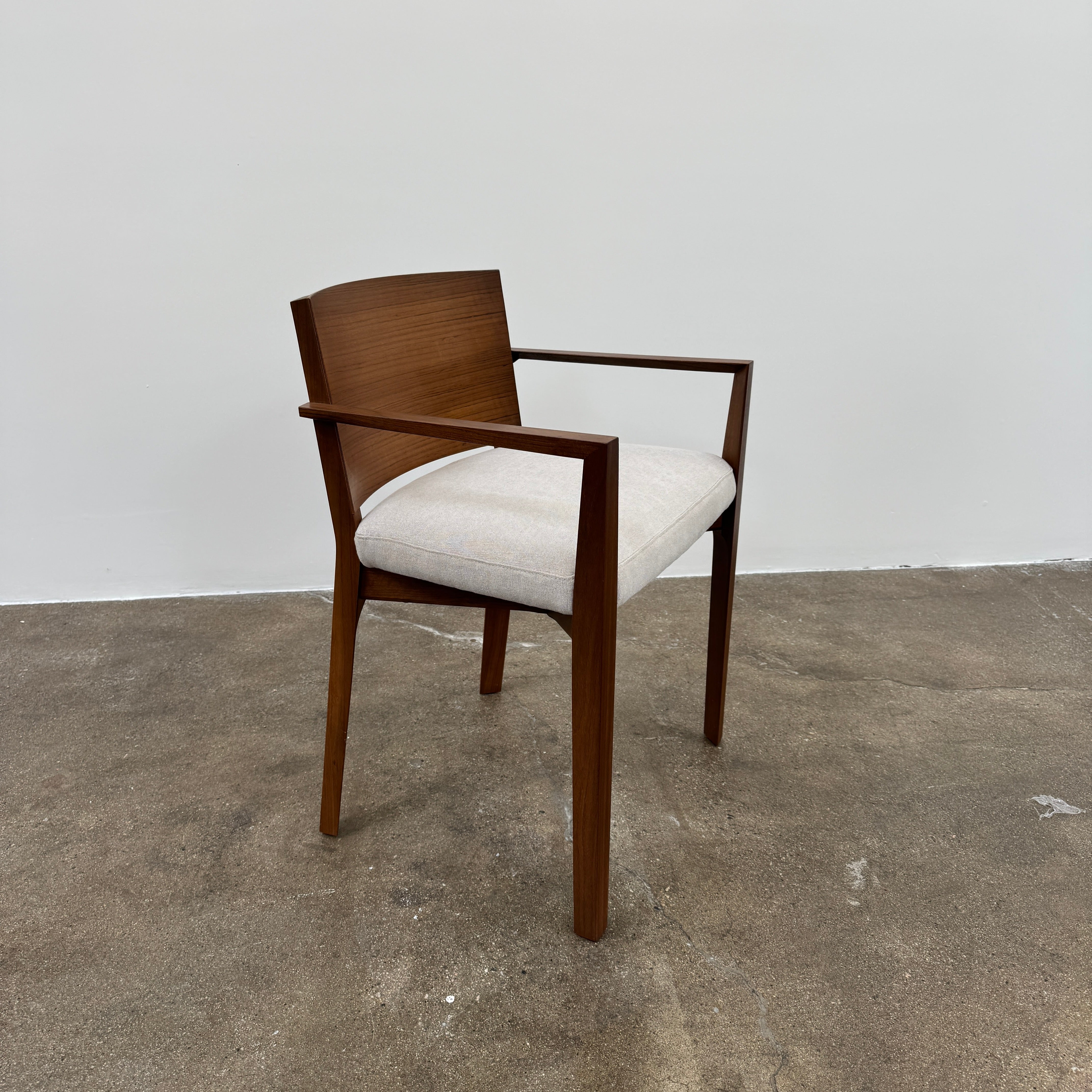 A set of 8 Porro Lario dining chairs by Porro, featuring minimalist armrests and light-cushioned seats, sits on a concrete floor against a plain white wall, reflecting refined contemporary style.