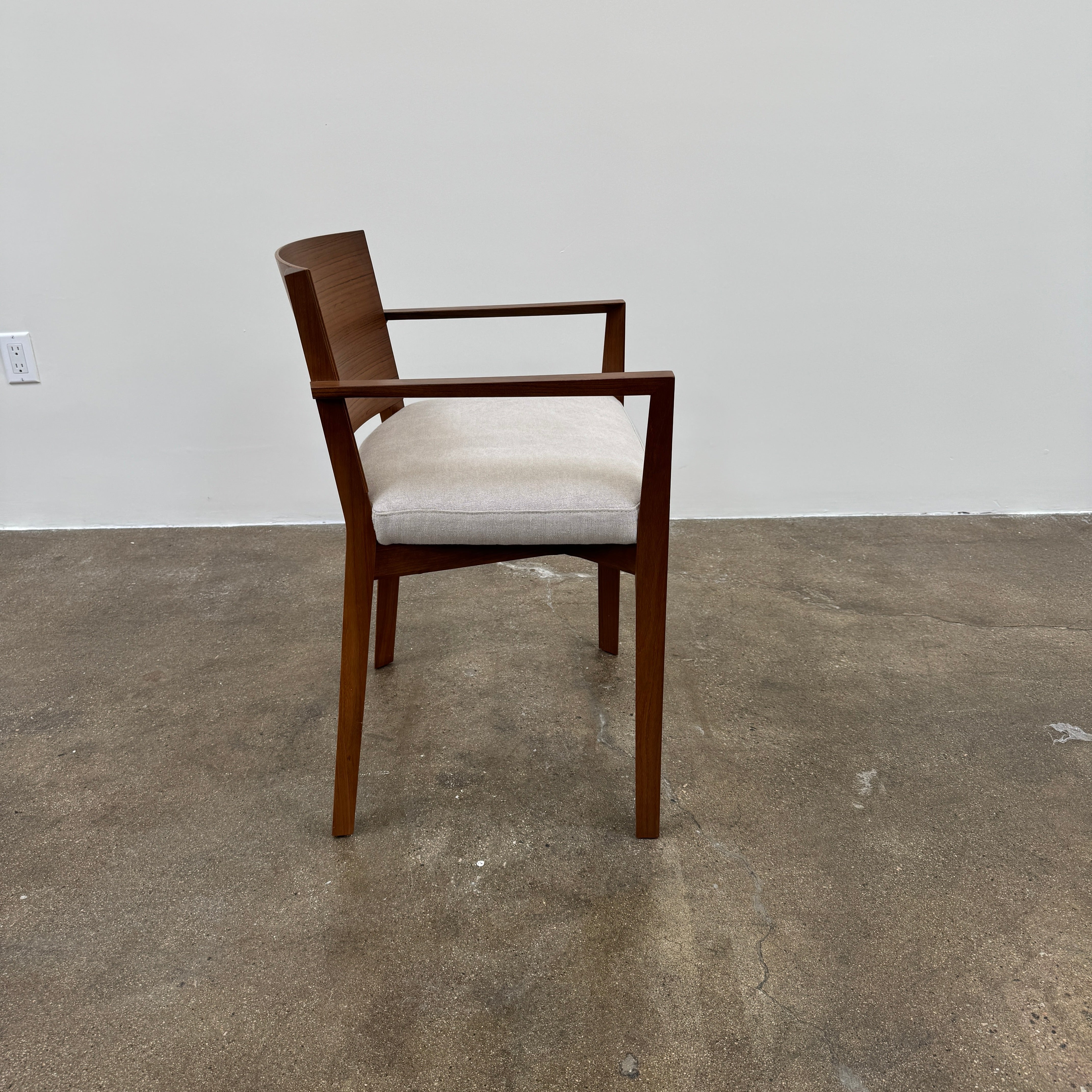 A set of 8 Porro Lario dining chairs by Porro, featuring minimalist armrests and light-cushioned seats, sits on a concrete floor against a plain white wall, reflecting refined contemporary style.