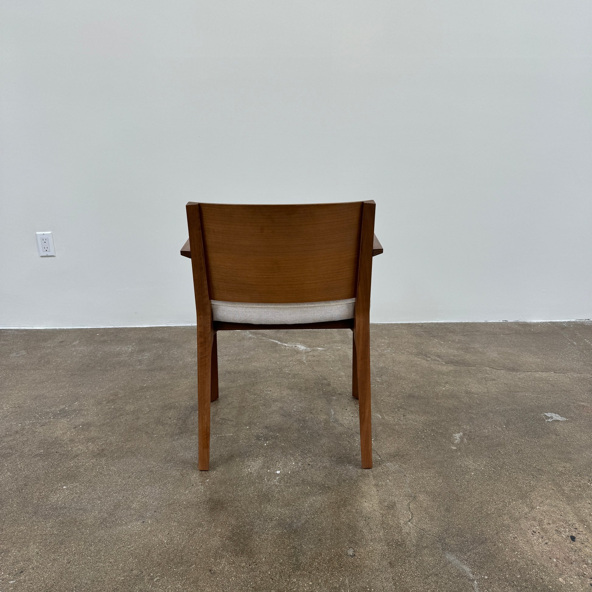 A set of 8 Porro Lario dining chairs by Porro, featuring minimalist armrests and light-cushioned seats, sits on a concrete floor against a plain white wall, reflecting refined contemporary style.