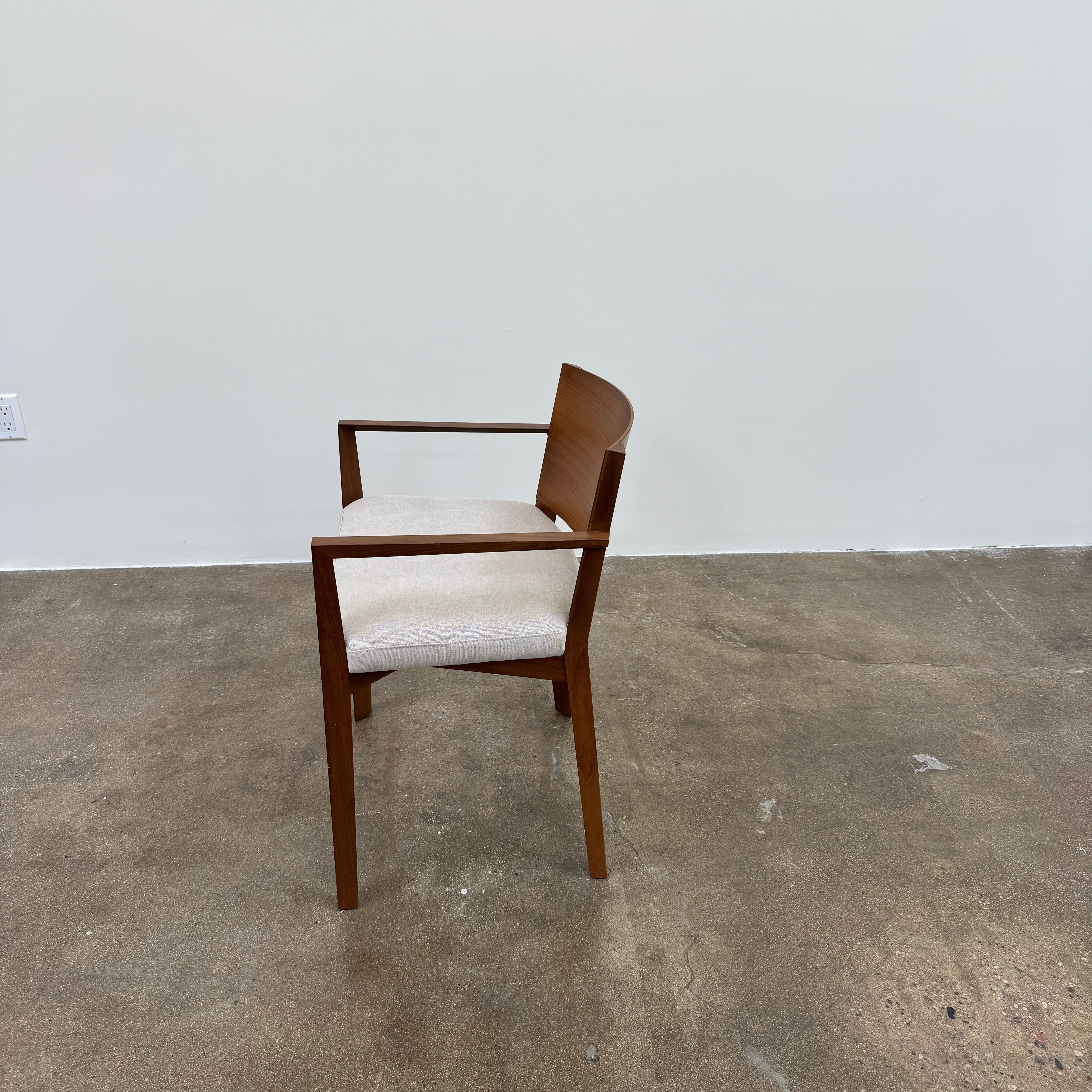 A set of 8 Porro Lario dining chairs by Porro, featuring minimalist armrests and light-cushioned seats, sits on a concrete floor against a plain white wall, reflecting refined contemporary style.