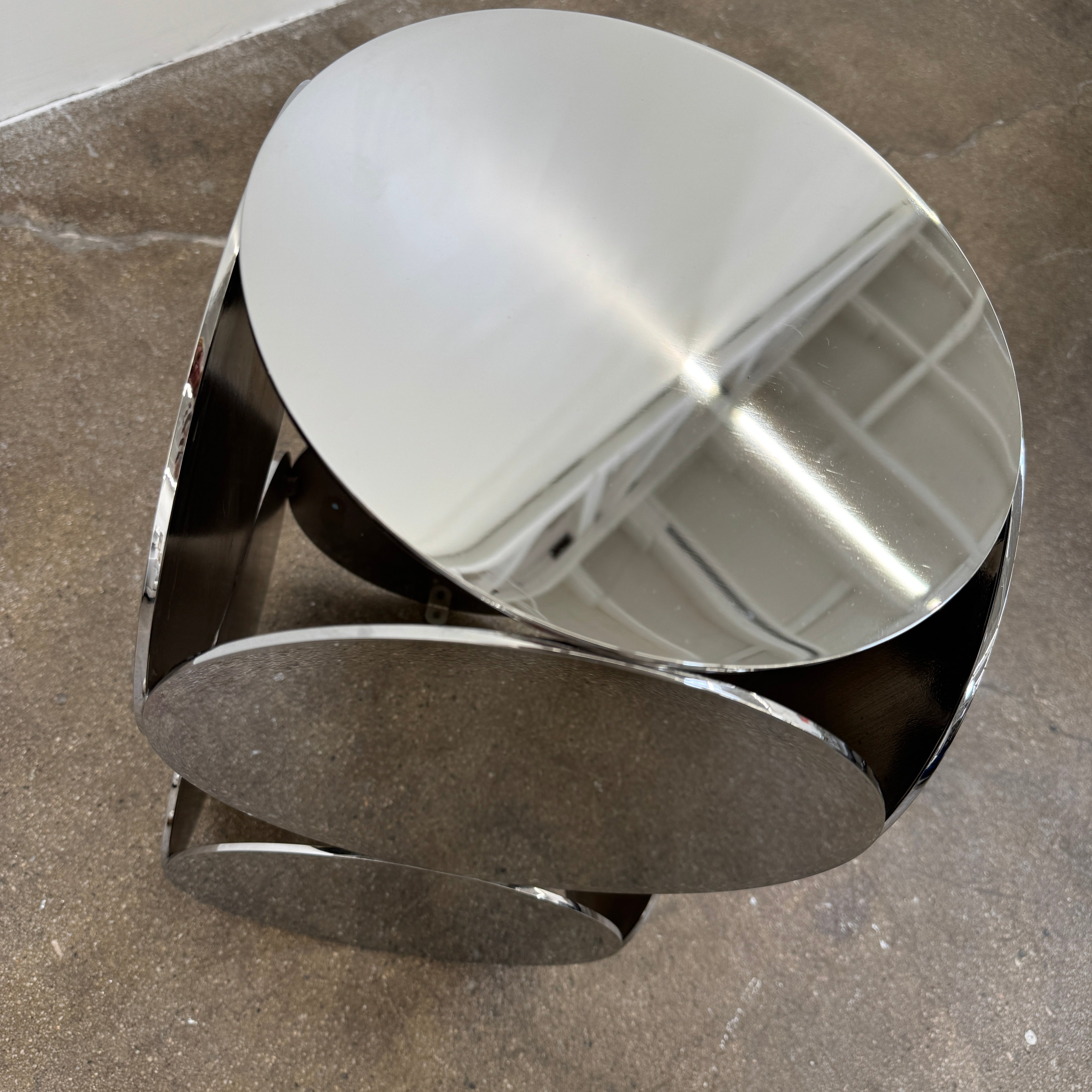 The Minotti Still Accent Table by Minotti features four large, circular, reflective metal discs stacked vertically for minimal elegance, shown on a concrete floor against a white wall.
