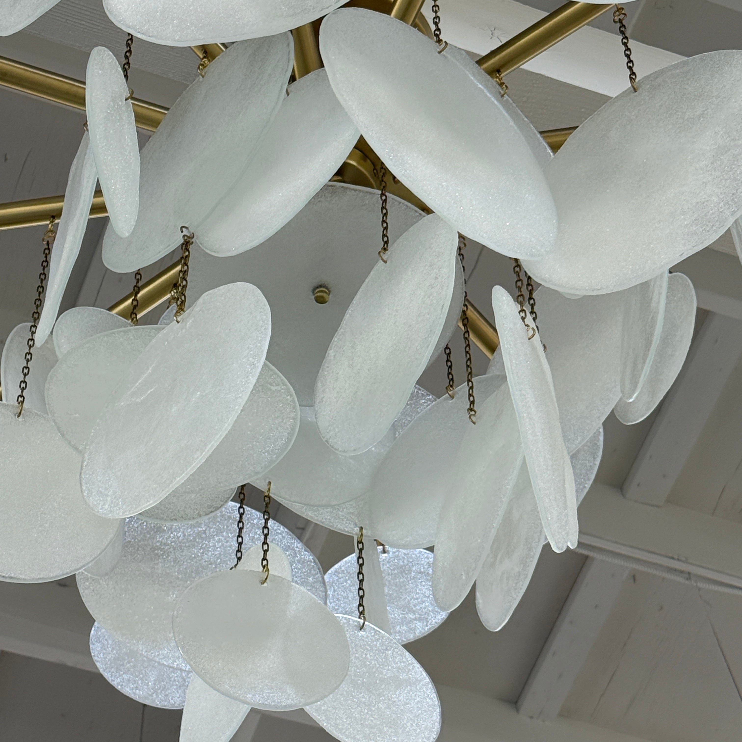 The Nimbu Medium Chandelier by Nimbu features a brass finish and layered frosted glass discs, creating a soft, warm glow—ideal as a contemporary centerpiece.