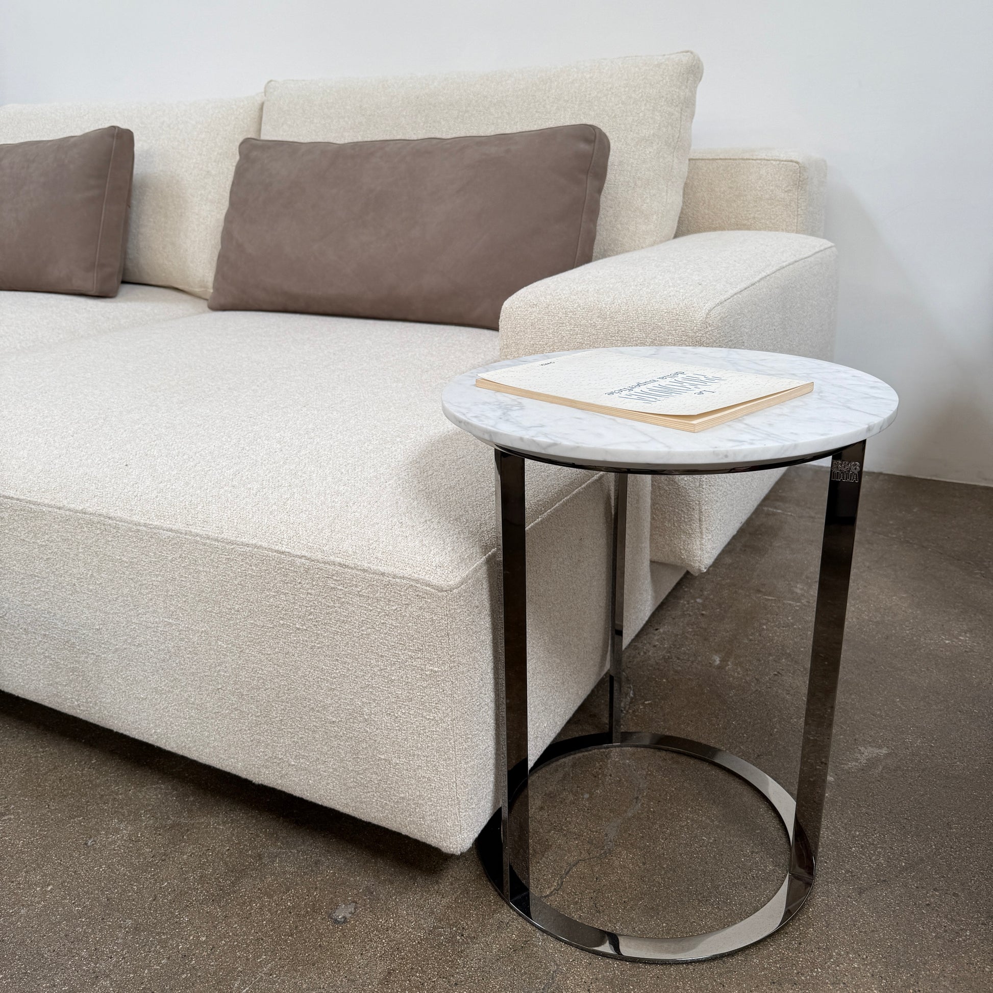 The B&B Italia Mera Accent Table features a round Carrara marble top and a three-legged metal frame with a circular base, showcasing B&B Italia's signature elegance.