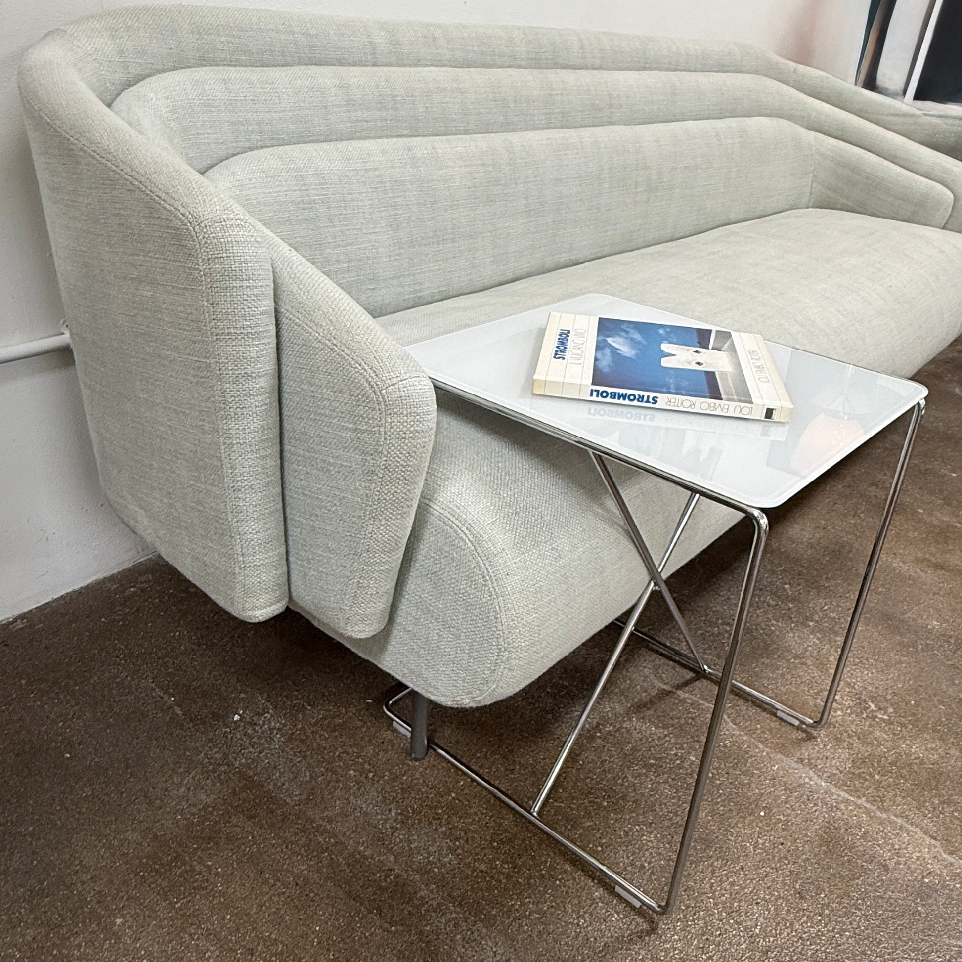 The B&B Italia JJ Cantilever Accent Table by B&B Italia features a white rectangular top and minimalist chrome frame, ideal for modern spaces. Shown against a plain white wall and black floor.