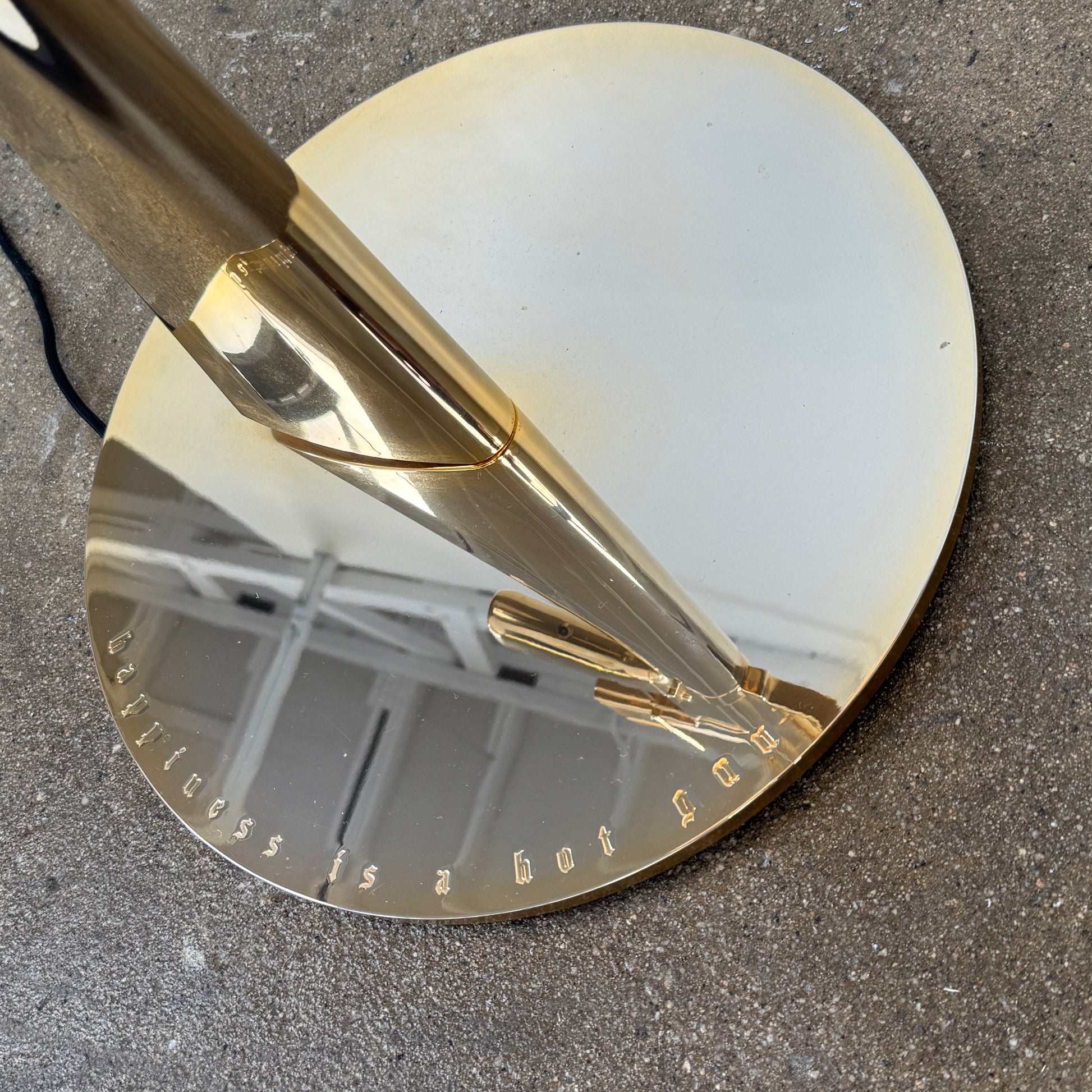 The Flos Guns Lounge Floor Lamp Gold by Flos features a shiny gold rifle-shaped base and a black lampshade, inspired by Philippe Starck, standing against a plain white background.