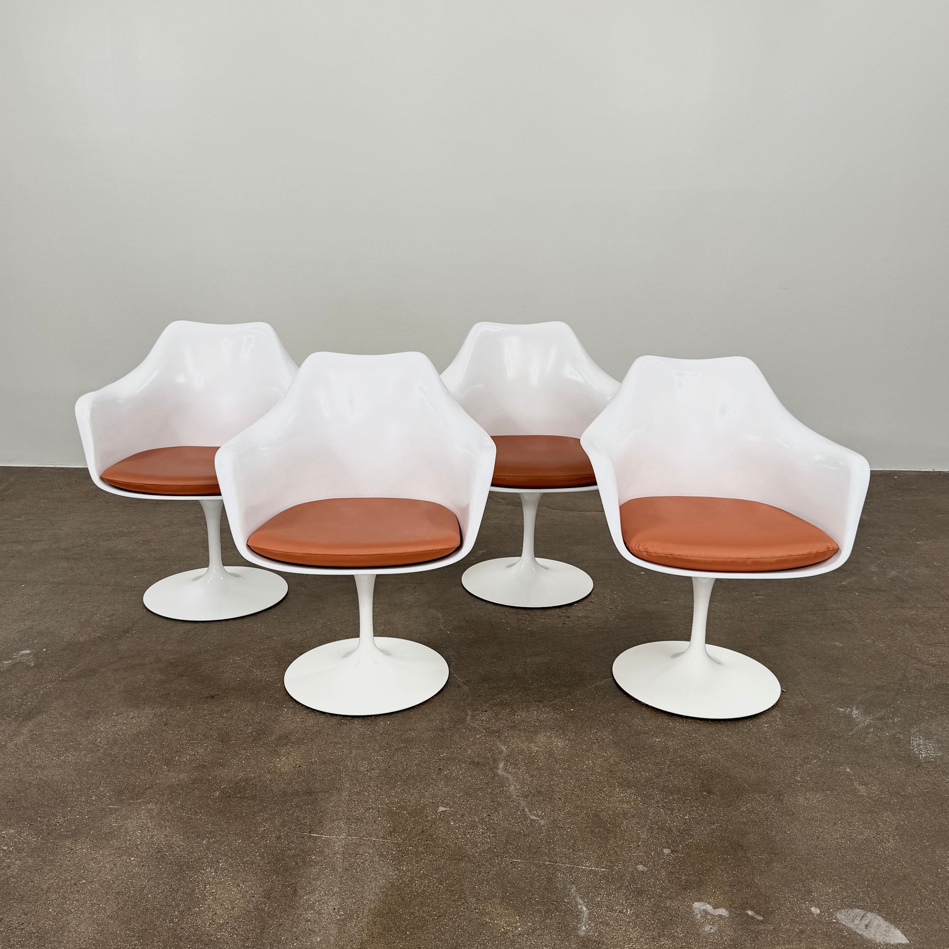 Four Knoll Saarinen Tulip Armchairs with brown vinyl seat cushions and pedestal bases, by Knoll, are arranged on a plain white background.