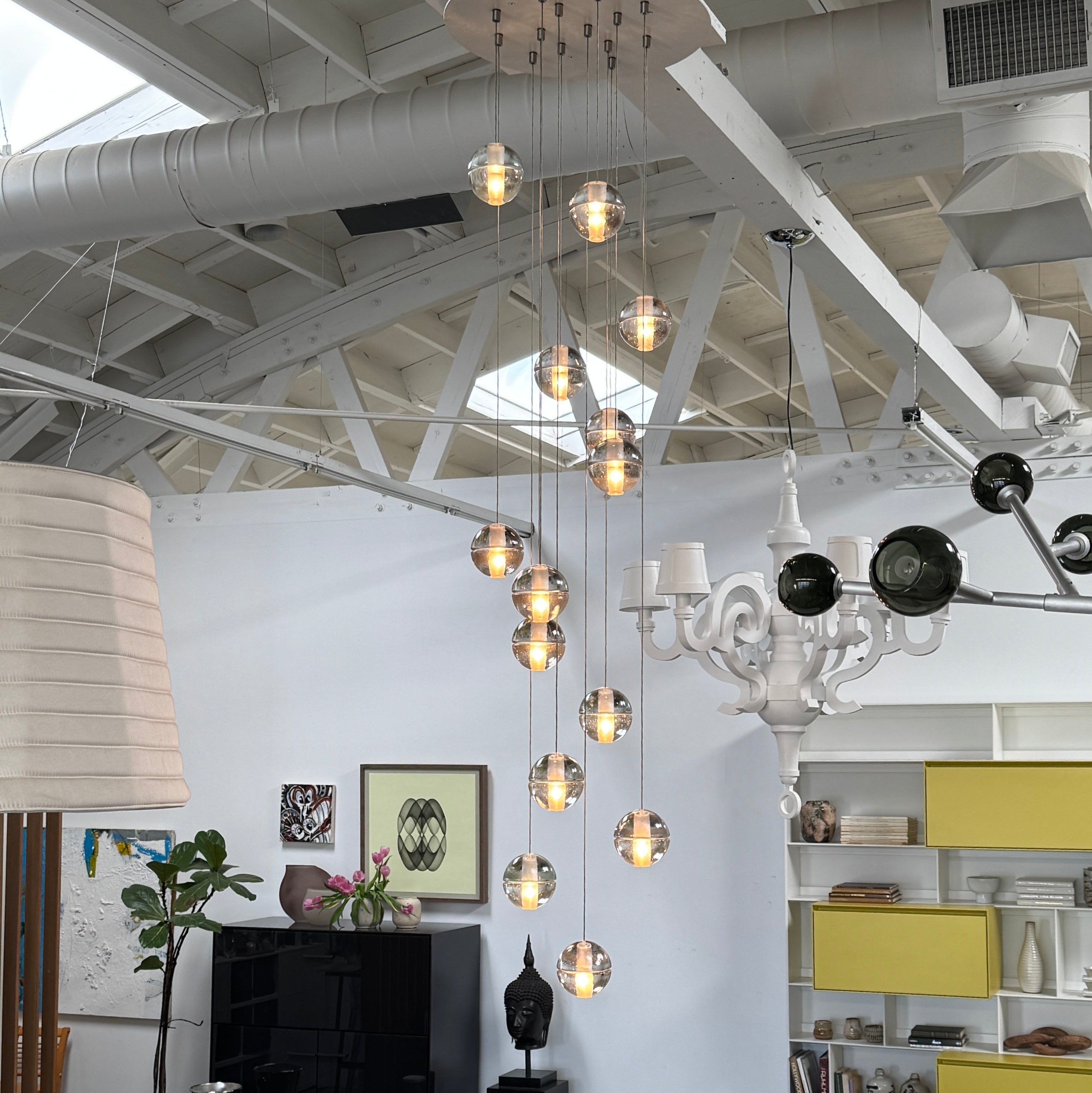 The Bocci 14.14 Pendant Chandelier by Bocci features a vertical cluster of metallic pendants, each with a glowing bulb, suspended by thin cords against a white background for a modern look.
