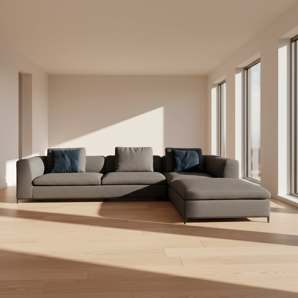 The B&B Italia Michele Club Sectional Sofa by B&B Italia, in dark grey open weave fabric with three seats and a right-side chaise lounge, sits on a concrete floor against a white wall—perfect for modern living spaces.