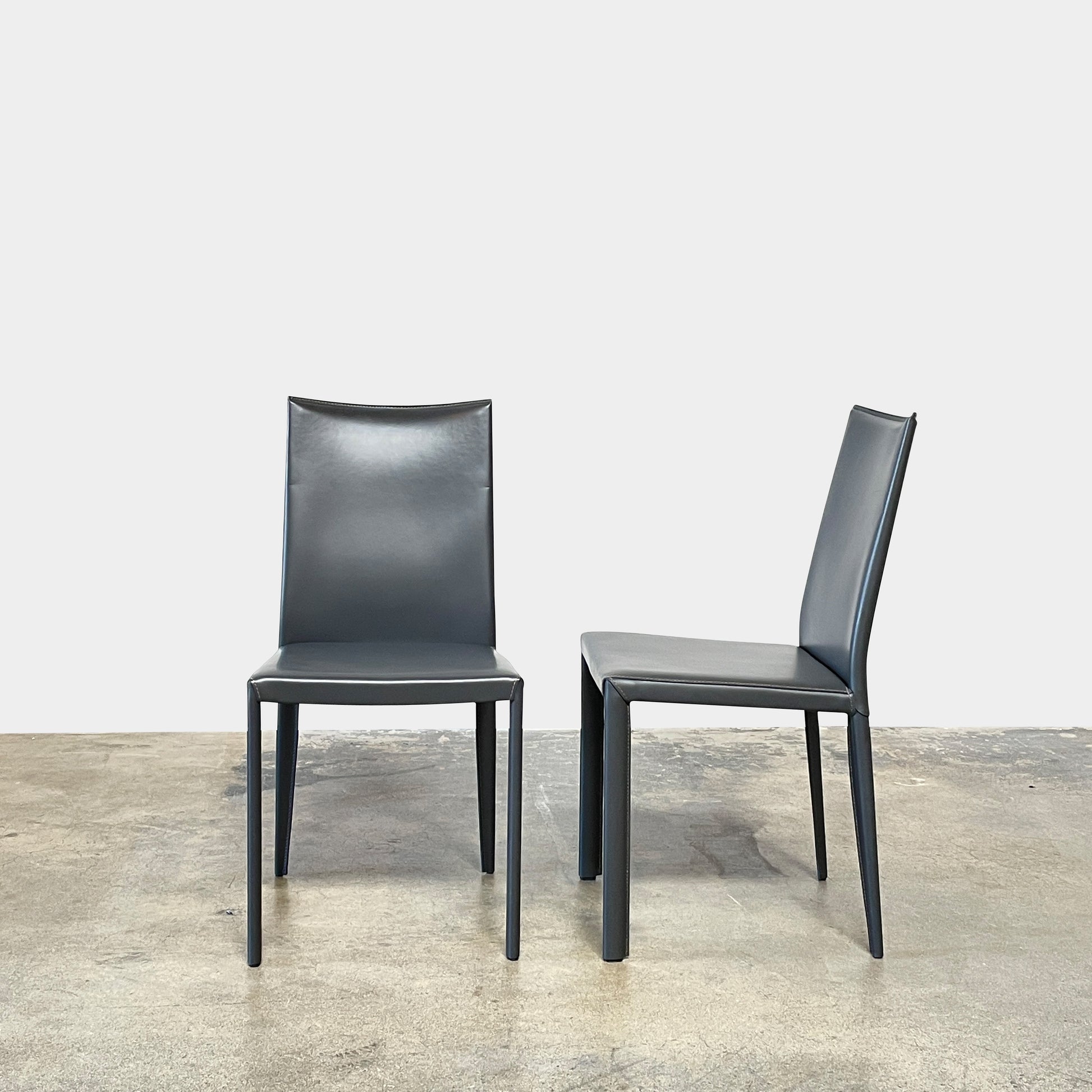Four Frag Bella Dining Chairs in Dark Grey Leather with metal legs, arranged in a straight line against a plain white background.