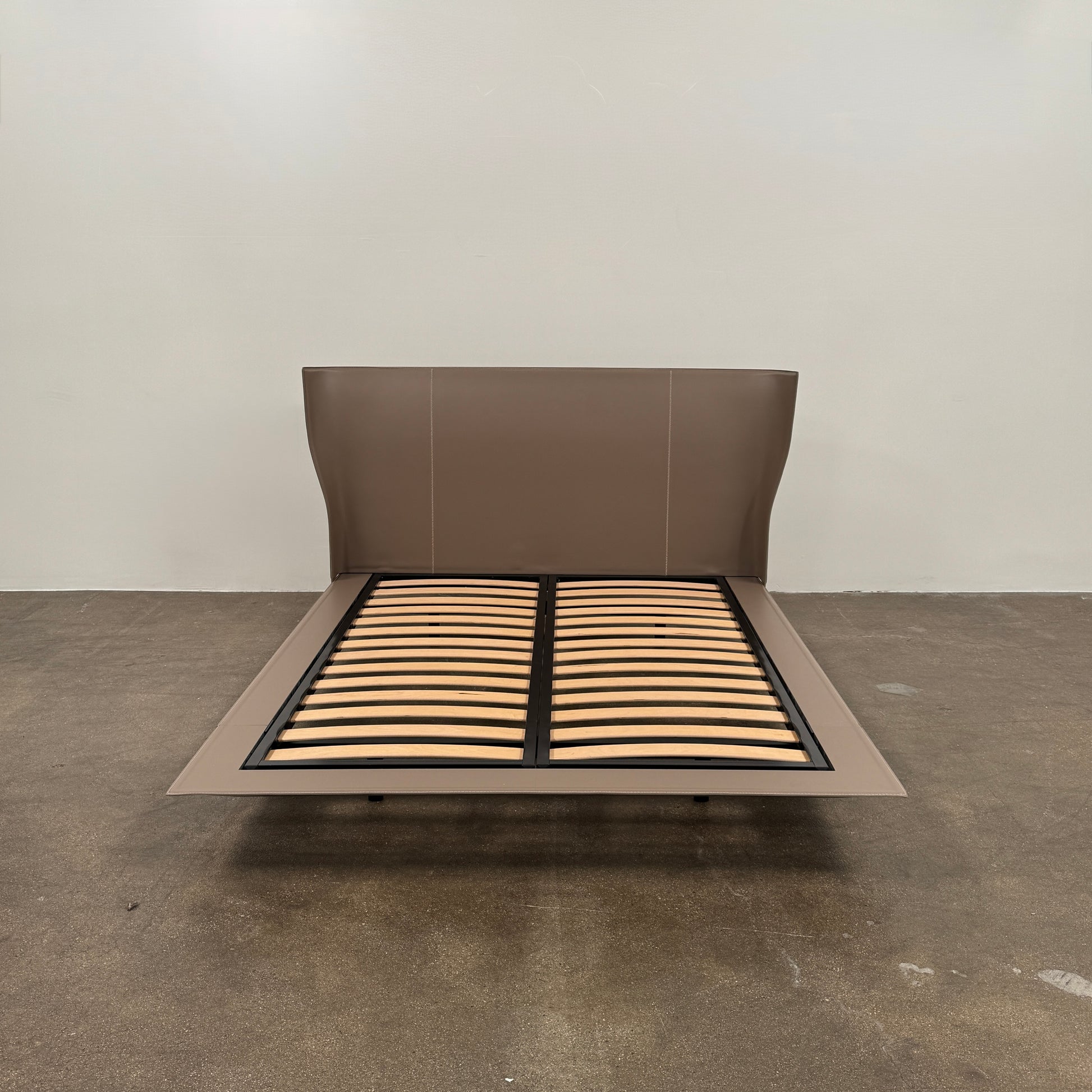 The B&B Italia Alys Queen Size Bed in Tortora Leather features a tall upholstered headboard and wooden slats, shown from a side angle against a plain background.