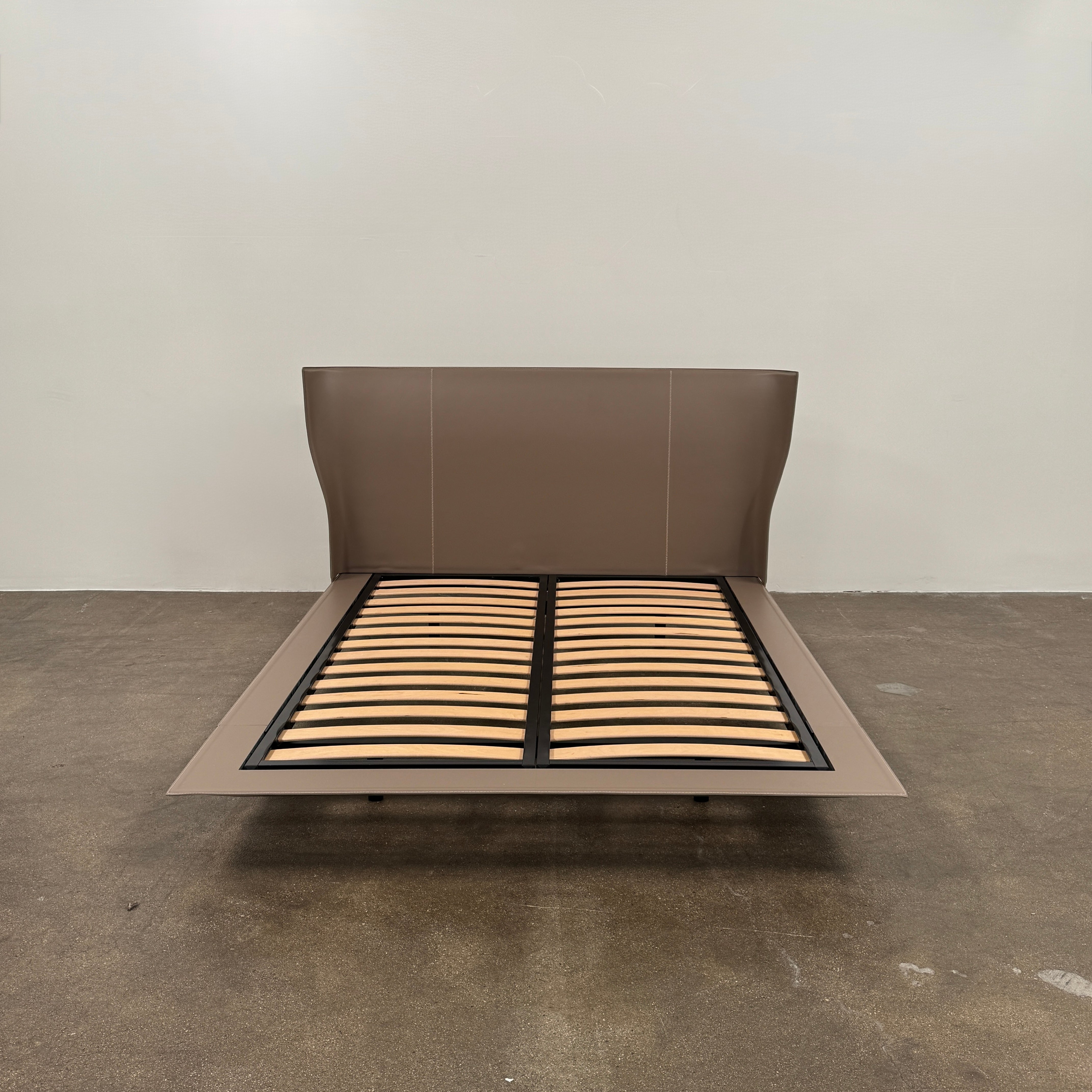 The B&B Italia Alys Queen Size Bed in Tortora Leather features a tall upholstered headboard and wooden slats, shown from a side angle against a plain background.
