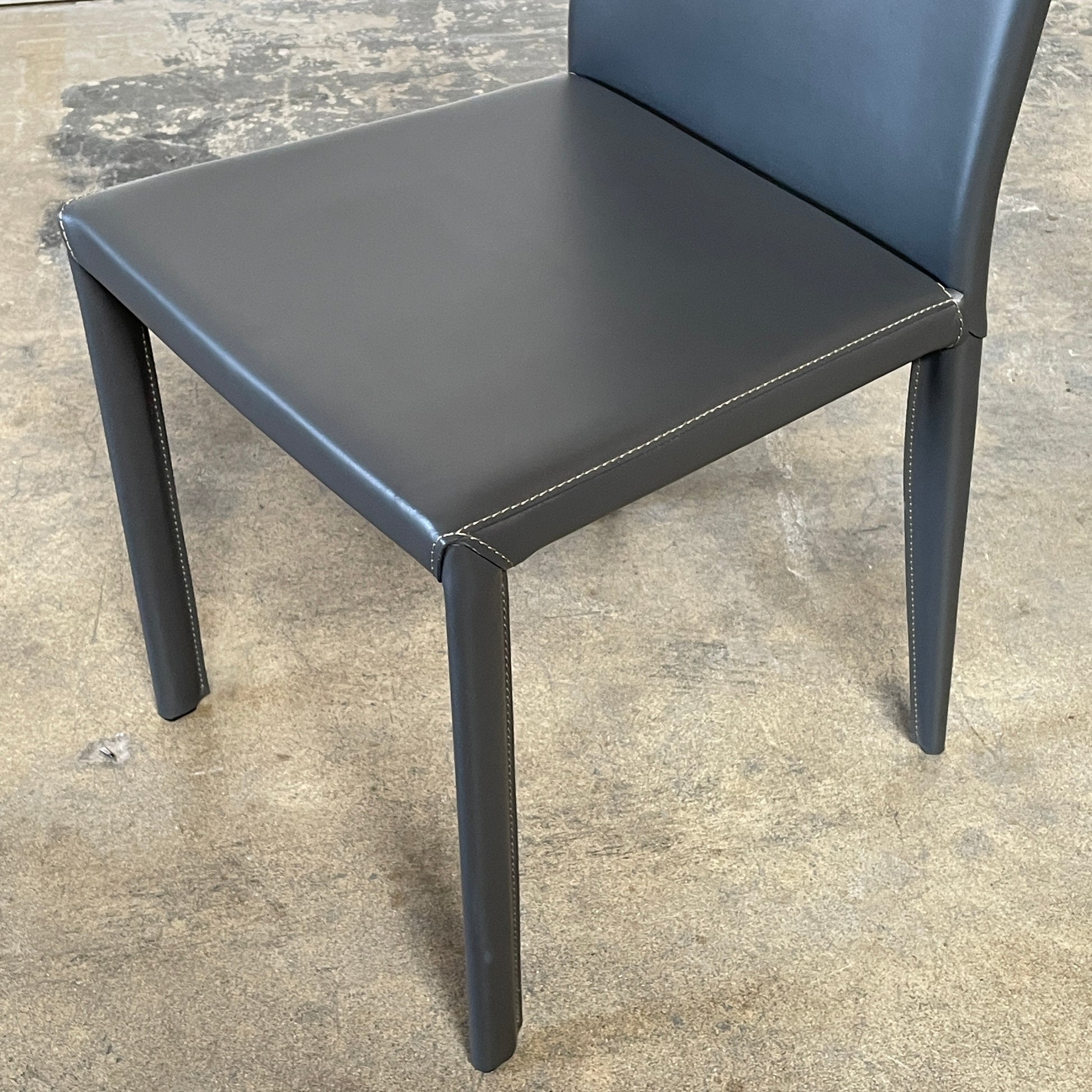 Four Frag Bella Dining Chairs in Dark Grey Leather with metal legs, arranged in a straight line against a plain white background.