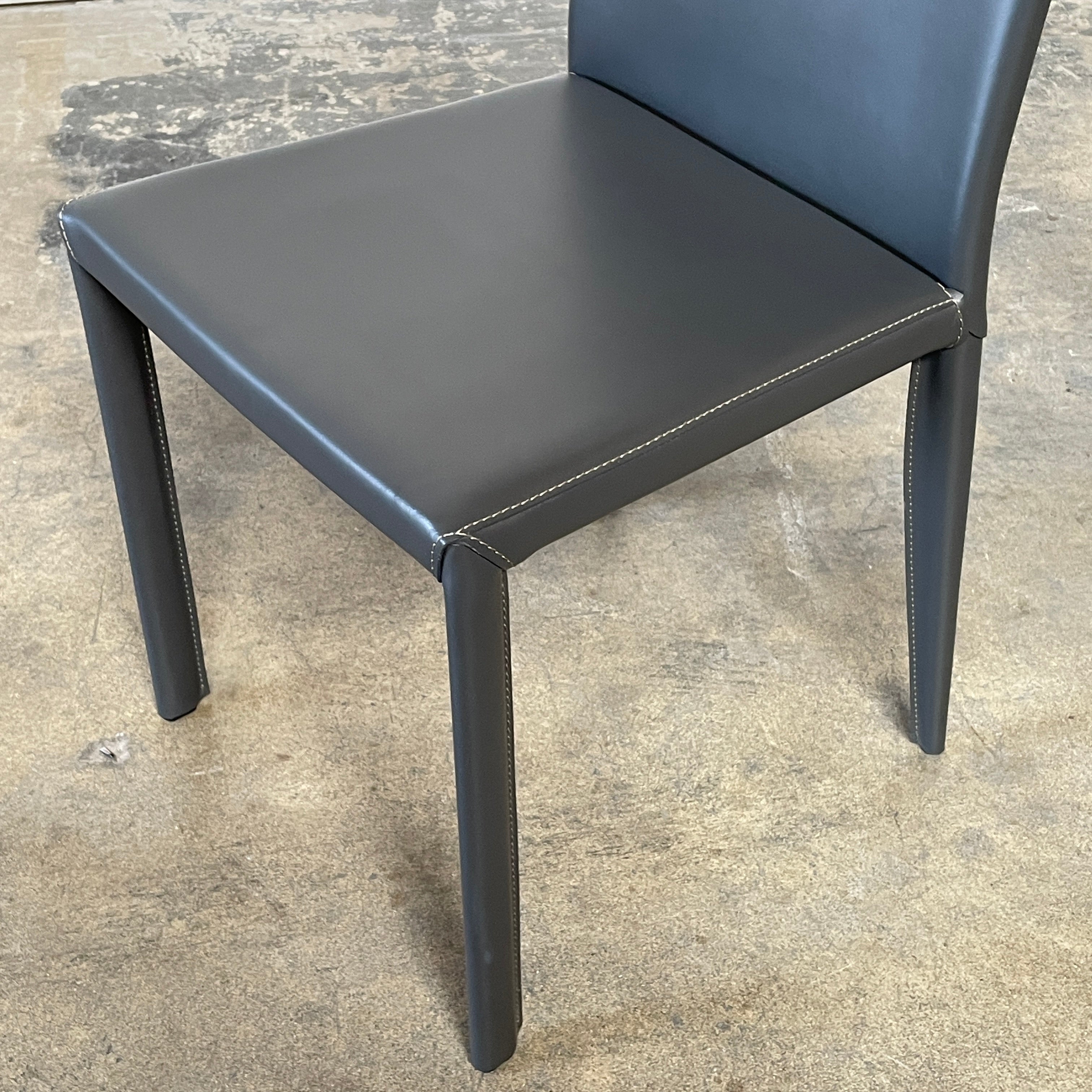 Four Frag Bella Dining Chairs in Dark Grey Leather with metal legs, arranged in a straight line against a plain white background.