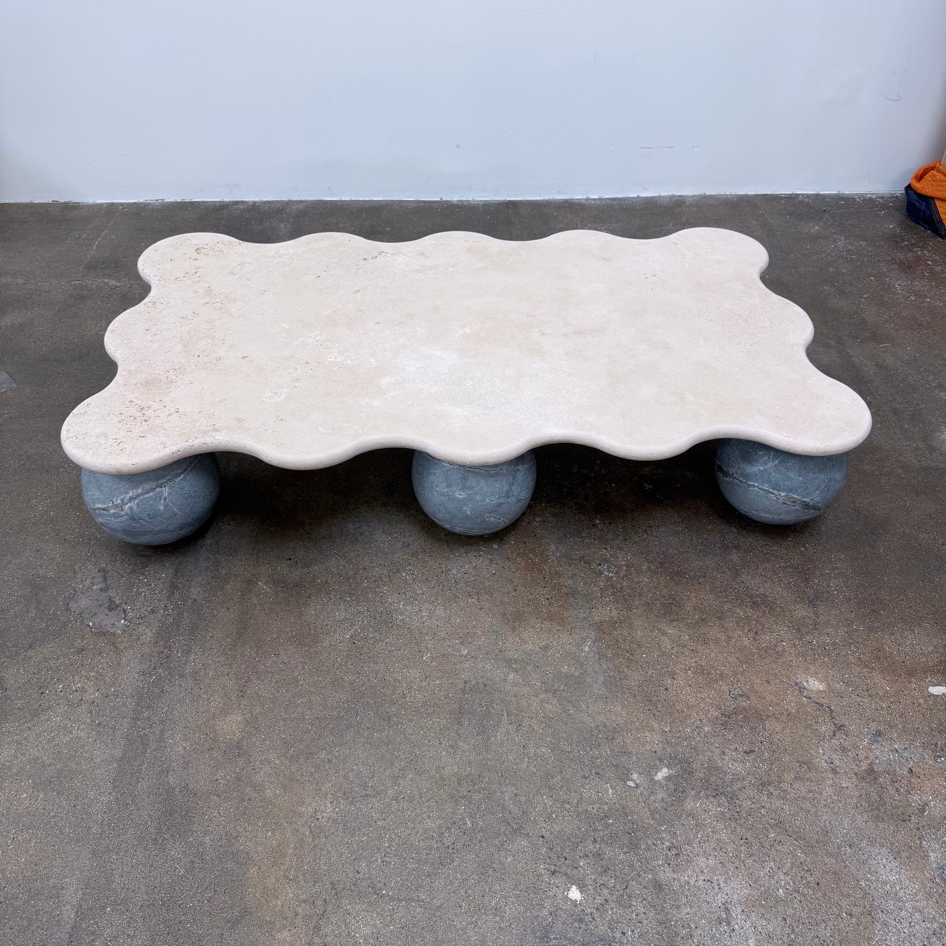 Form(LA) Palla Rectangle Coffee Table with a wavy-edged stone top supported by three spherical stone legs.