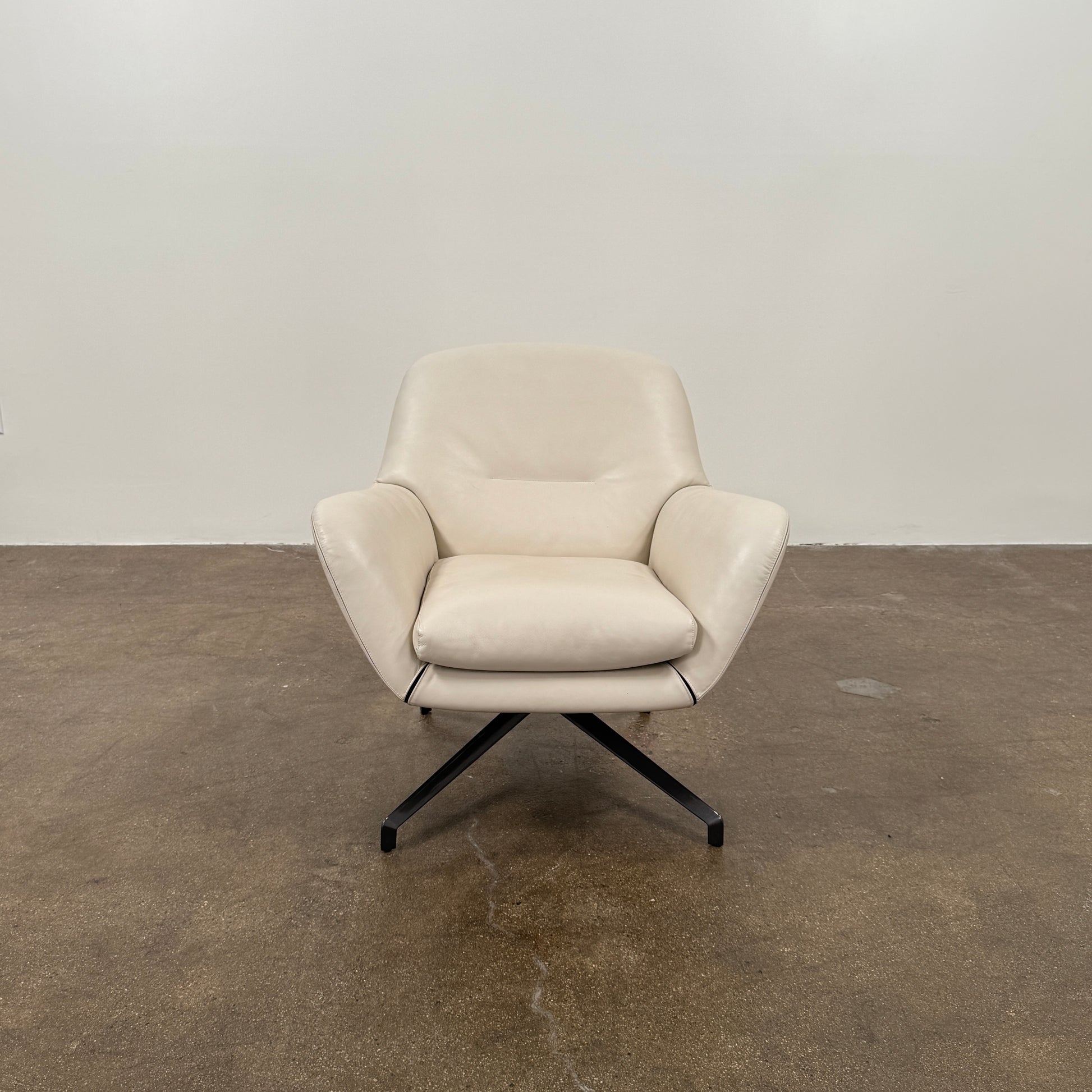 Two modern Minotti Jensen Swivel Chairs by Minotti face each other in a bright room with large windows overlooking the city, pale wood floors, and minimal decor for a contemporary, sophisticated look.