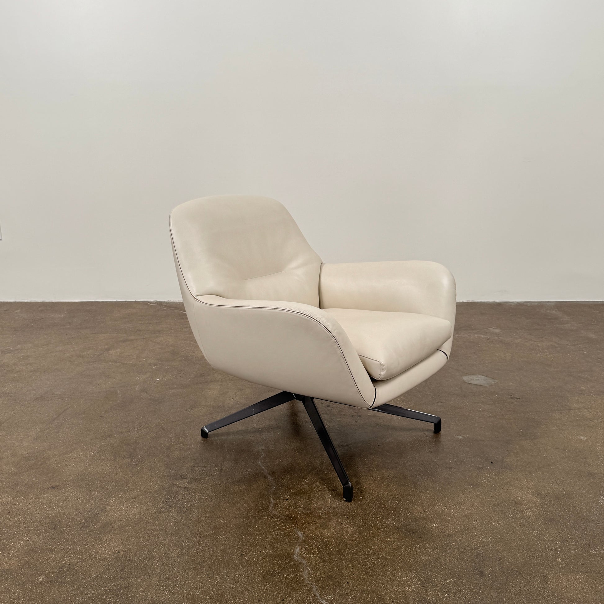 Two modern Minotti Jensen Swivel Chairs by Minotti face each other in a bright room with large windows overlooking the city, pale wood floors, and minimal decor for a contemporary, sophisticated look.