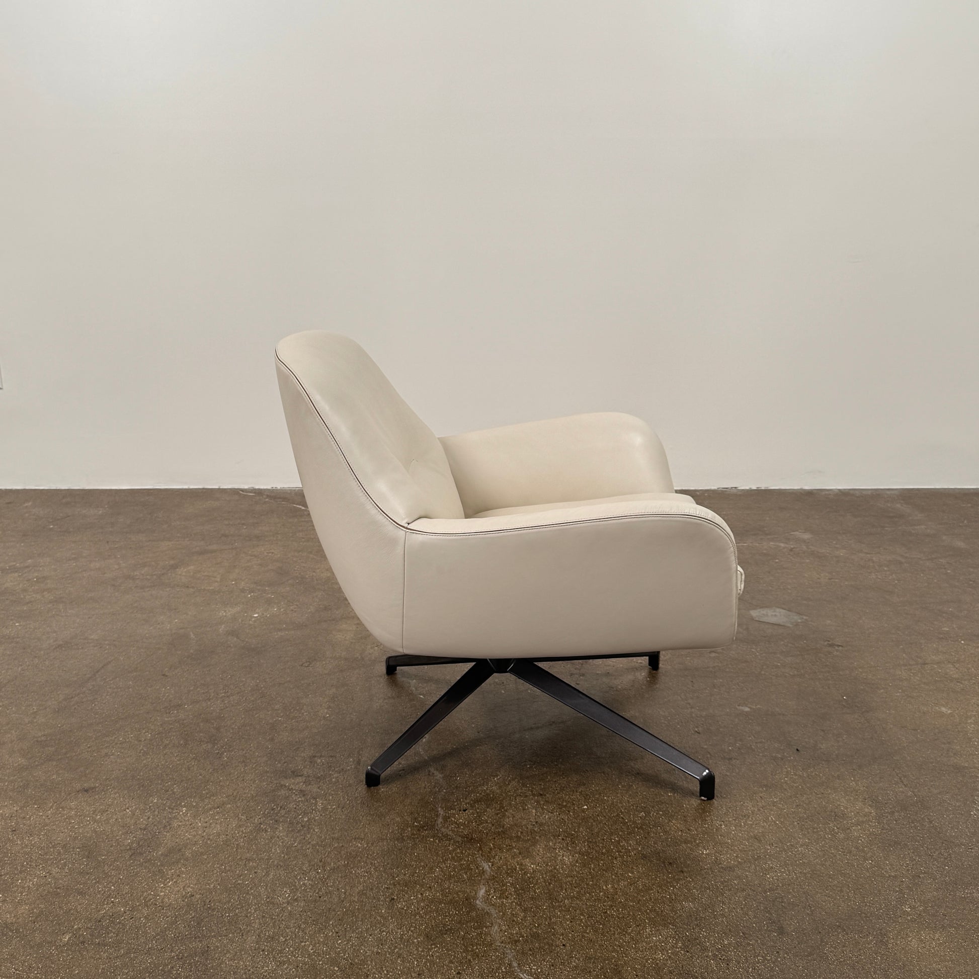 Two modern Minotti Jensen Swivel Chairs by Minotti face each other in a bright room with large windows overlooking the city, pale wood floors, and minimal decor for a contemporary, sophisticated look.