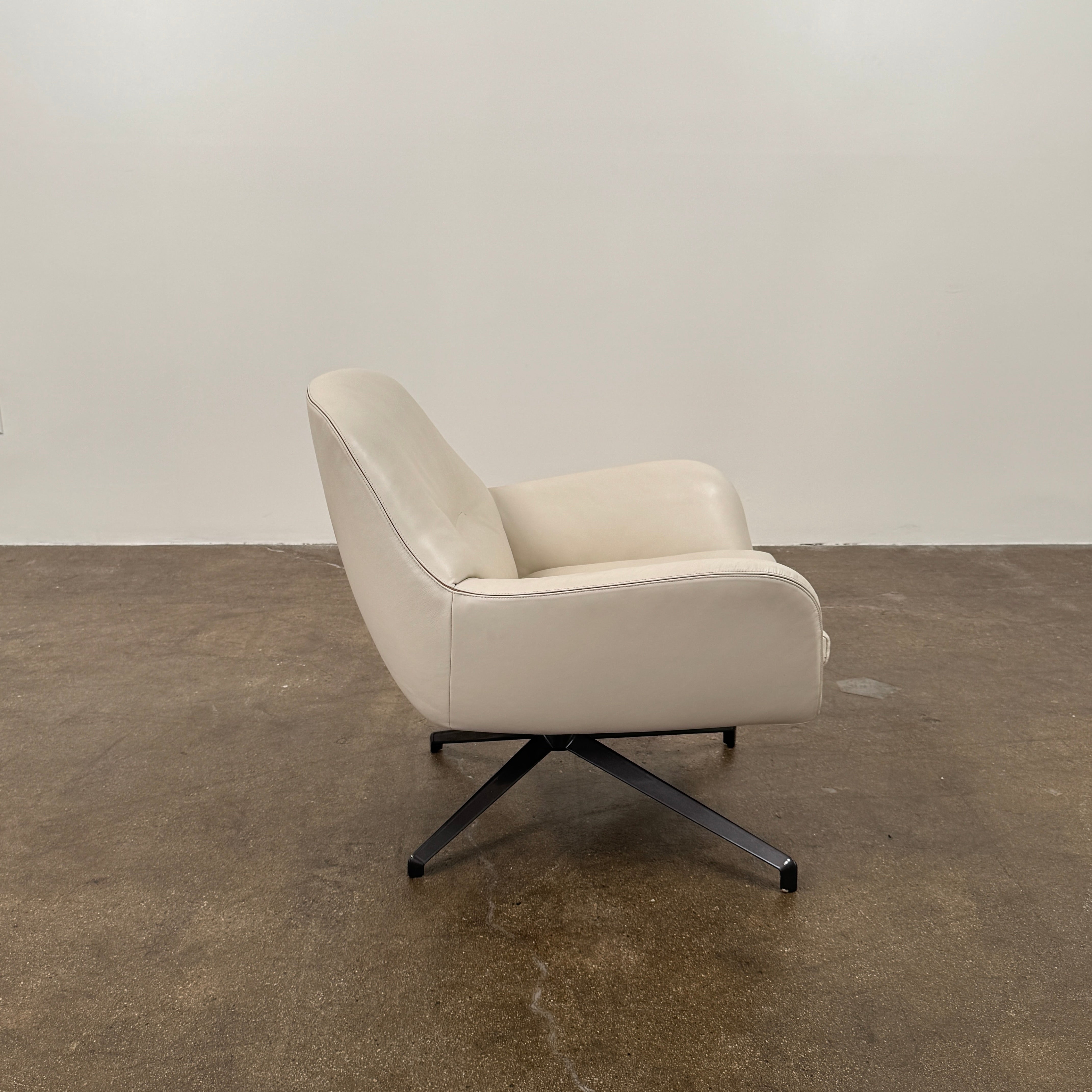 Two modern Minotti Jensen Swivel Chairs by Minotti face each other in a bright room with large windows overlooking the city, pale wood floors, and minimal decor for a contemporary, sophisticated look.