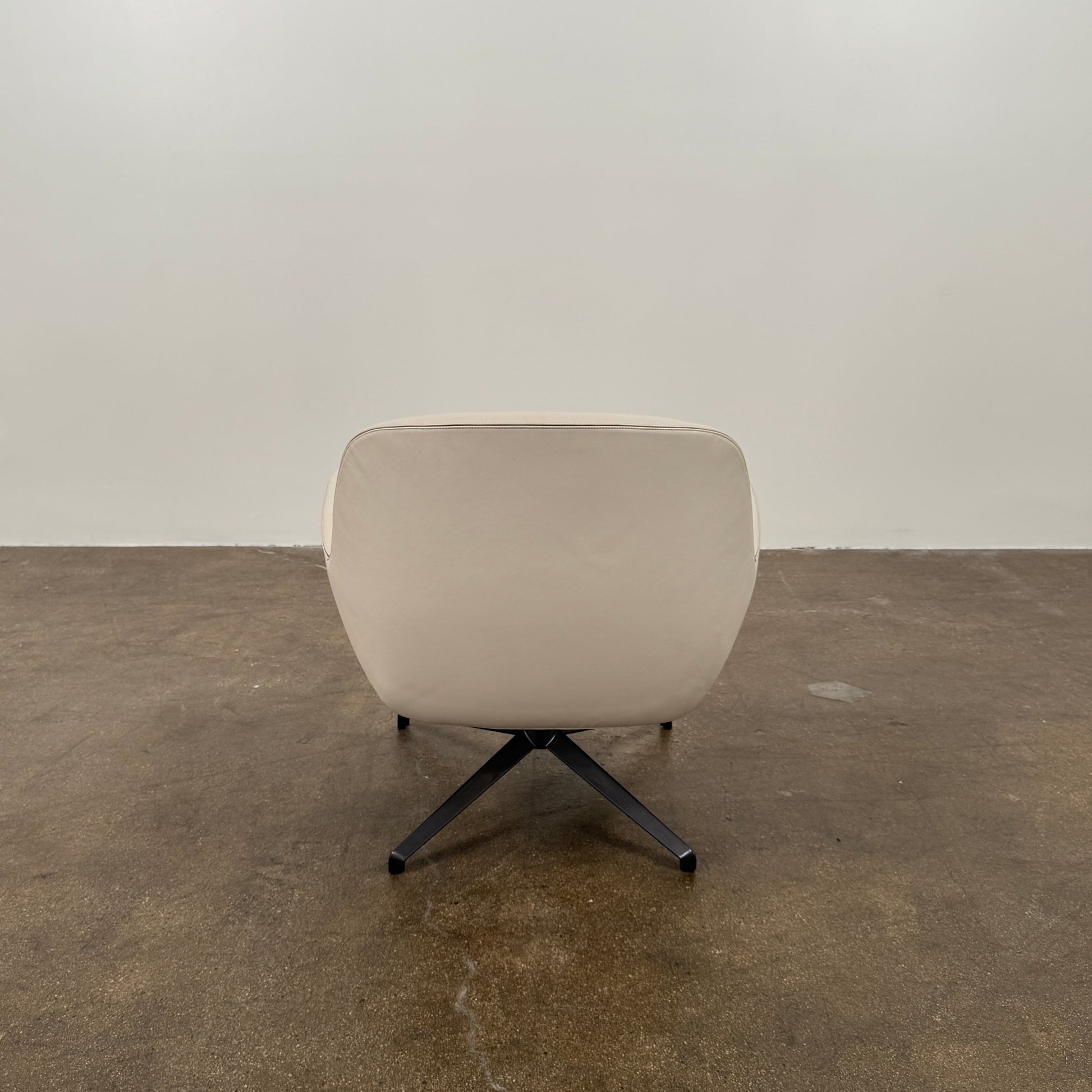 Two modern Minotti Jensen Swivel Chairs by Minotti face each other in a bright room with large windows overlooking the city, pale wood floors, and minimal decor for a contemporary, sophisticated look.