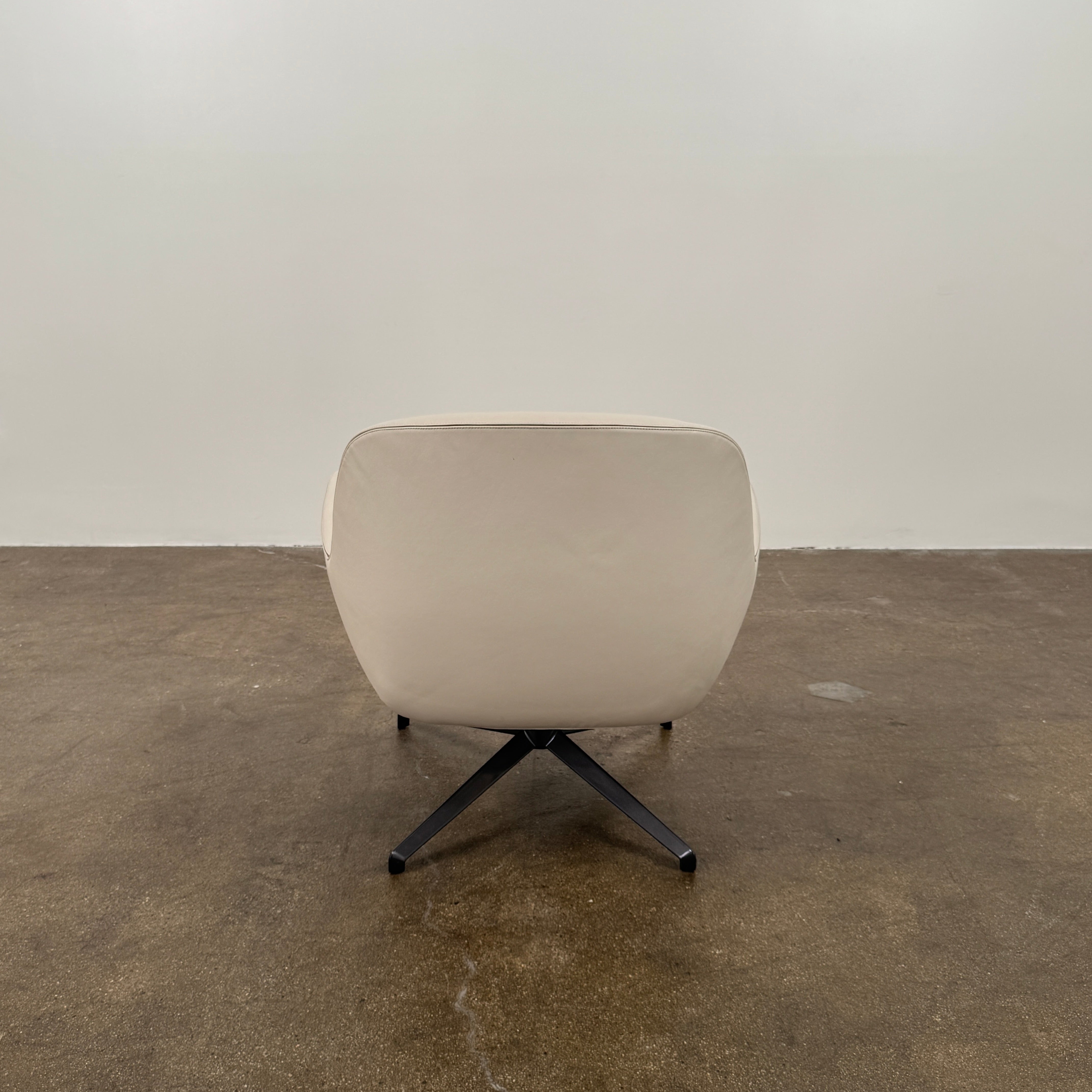 Two modern Minotti Jensen Swivel Chairs by Minotti face each other in a bright room with large windows overlooking the city, pale wood floors, and minimal decor for a contemporary, sophisticated look.