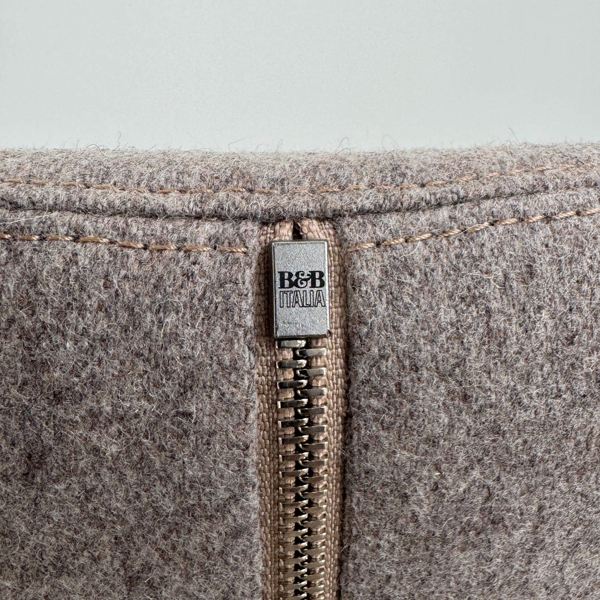 The B&B Italia Mini Papilio Swivel Chair features curved armrests and light brown upholstery, elegantly set on a polished concrete floor against a plain white wall.