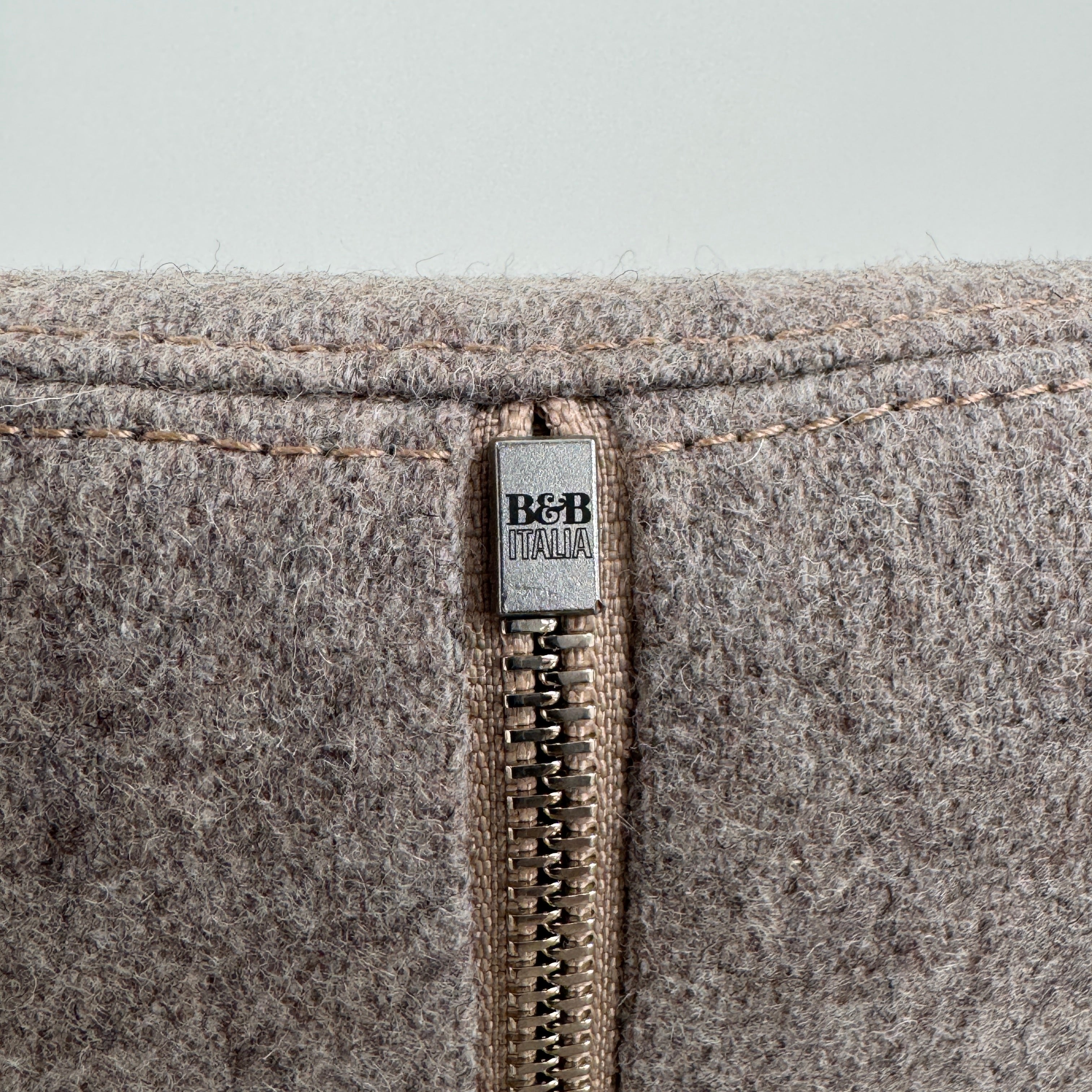 The B&B Italia Mini Papilio Swivel Chair features curved armrests and light brown upholstery, elegantly set on a polished concrete floor against a plain white wall.