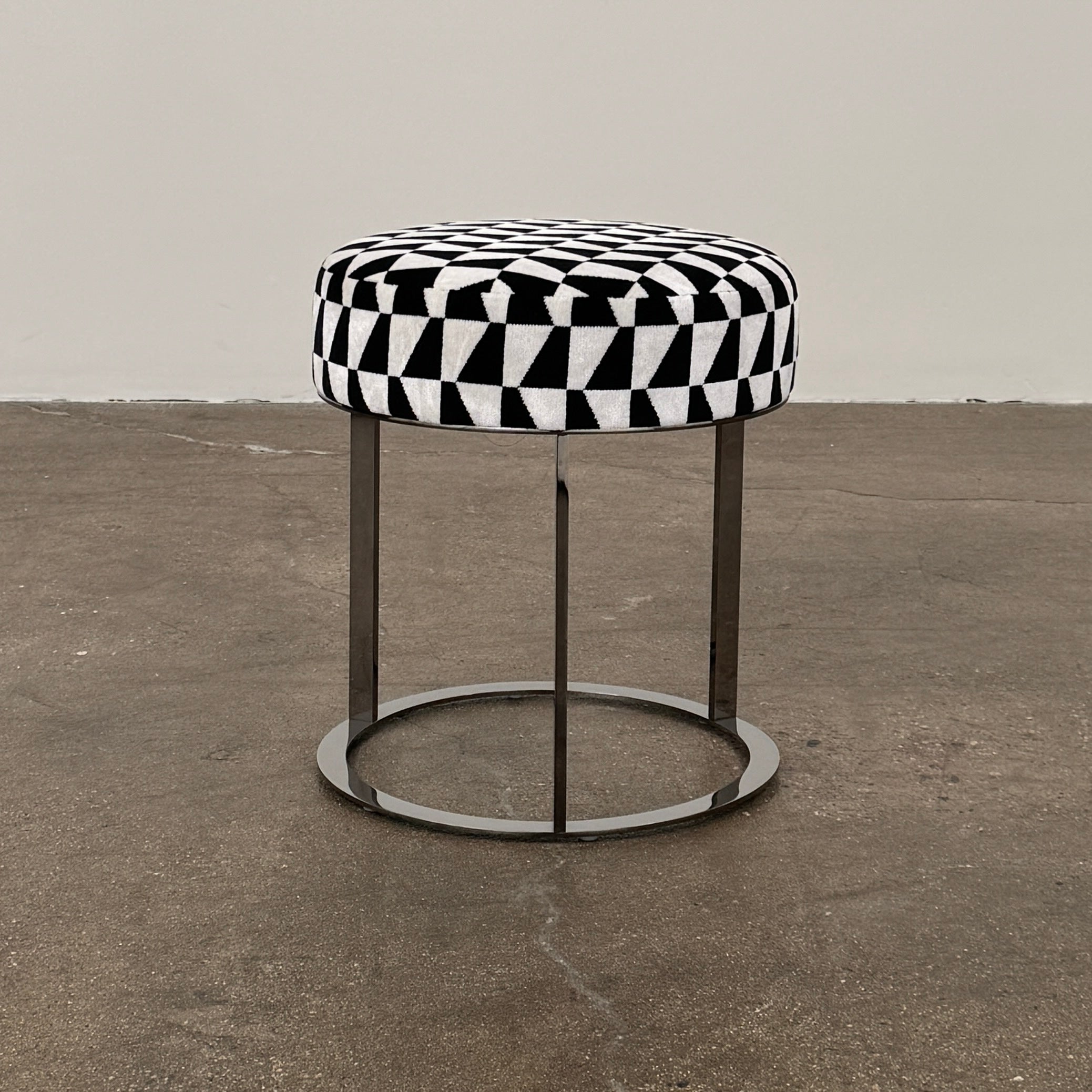 The B&B Italia Frank Ottoman features a black and white geometric cushion on a metal base with three vertical supports and a circular footrest.