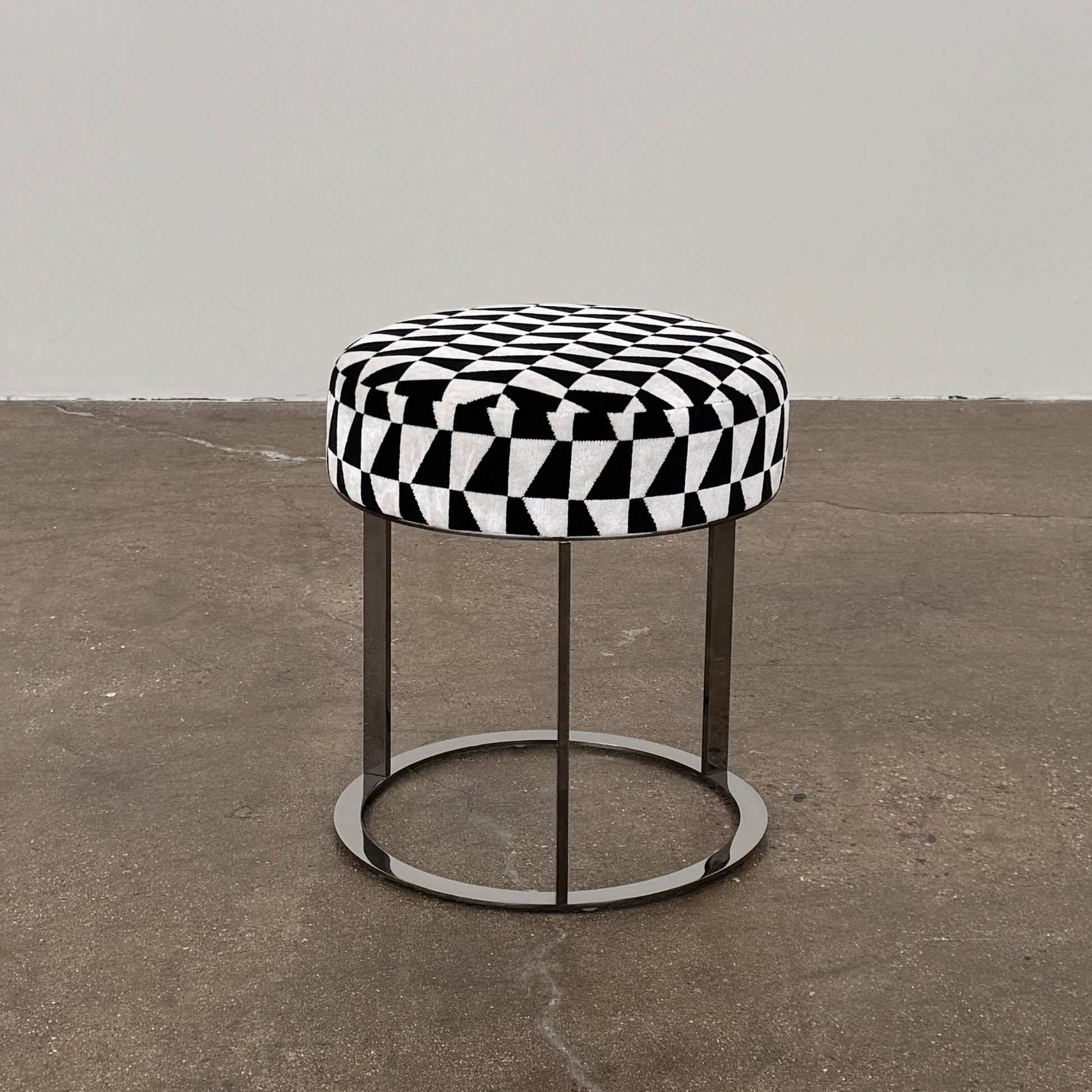 The B&B Italia Frank Ottoman features a black and white geometric cushion on a metal base with three vertical supports and a circular footrest.