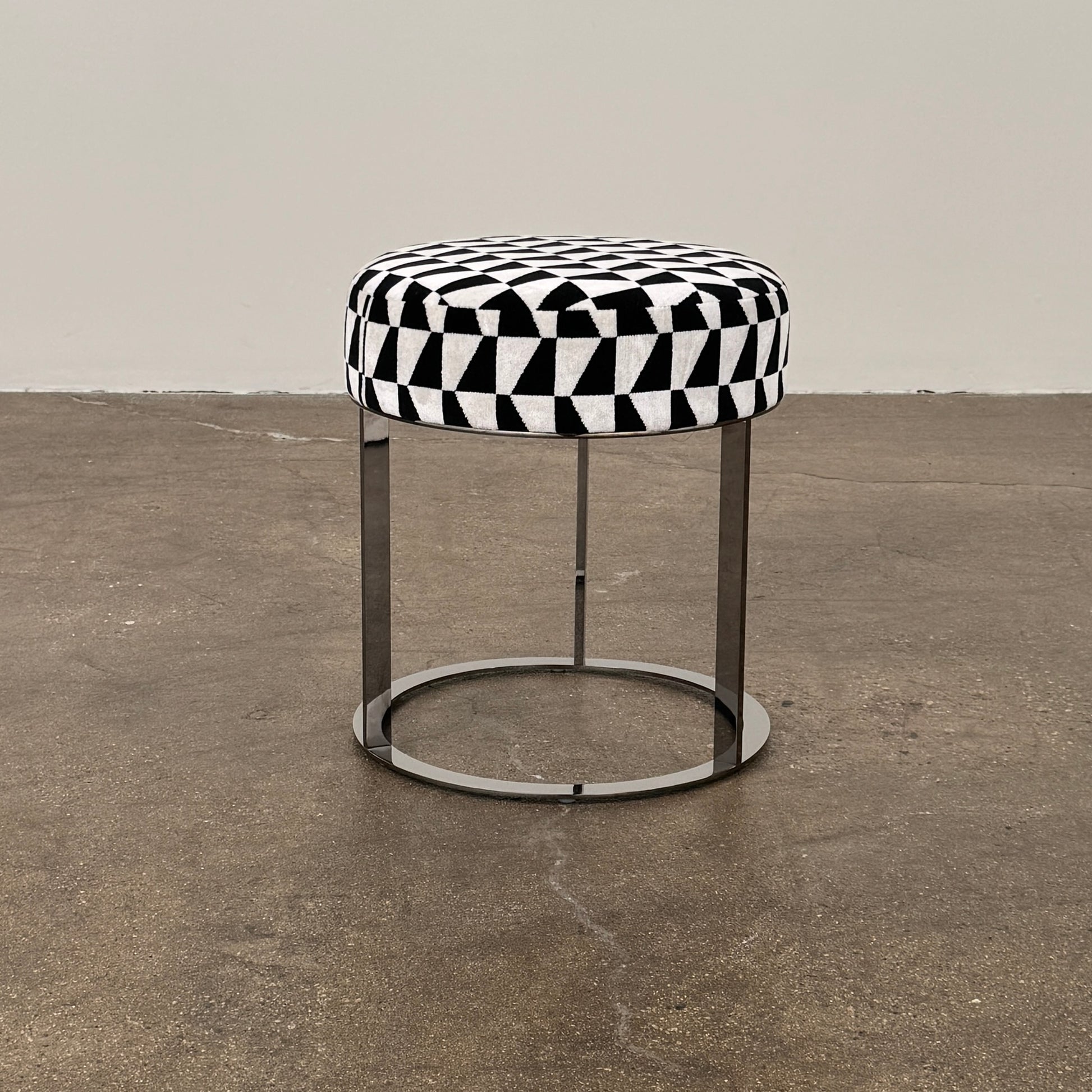 The B&B Italia Frank Ottoman features a black and white geometric cushion on a metal base with three vertical supports and a circular footrest.