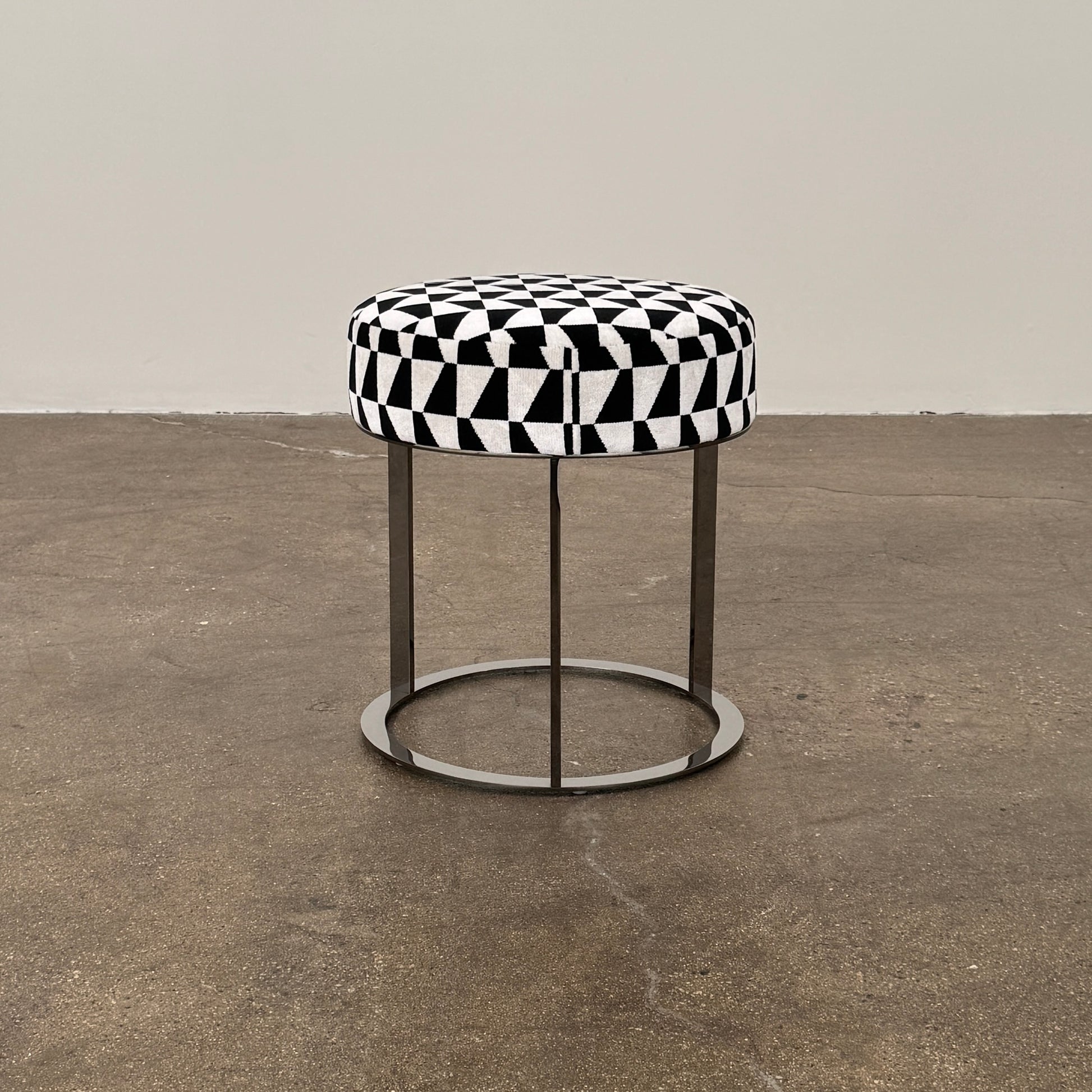 The B&B Italia Frank Ottoman features a black and white geometric cushion on a metal base with three vertical supports and a circular footrest.